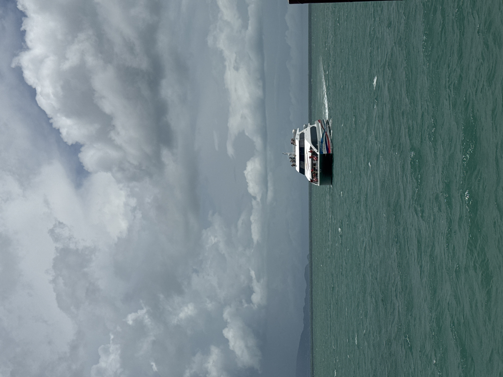 A ferry travels across the water under a cloudy sky. It is likely near Thong Sala, Thailand, given the prompt.