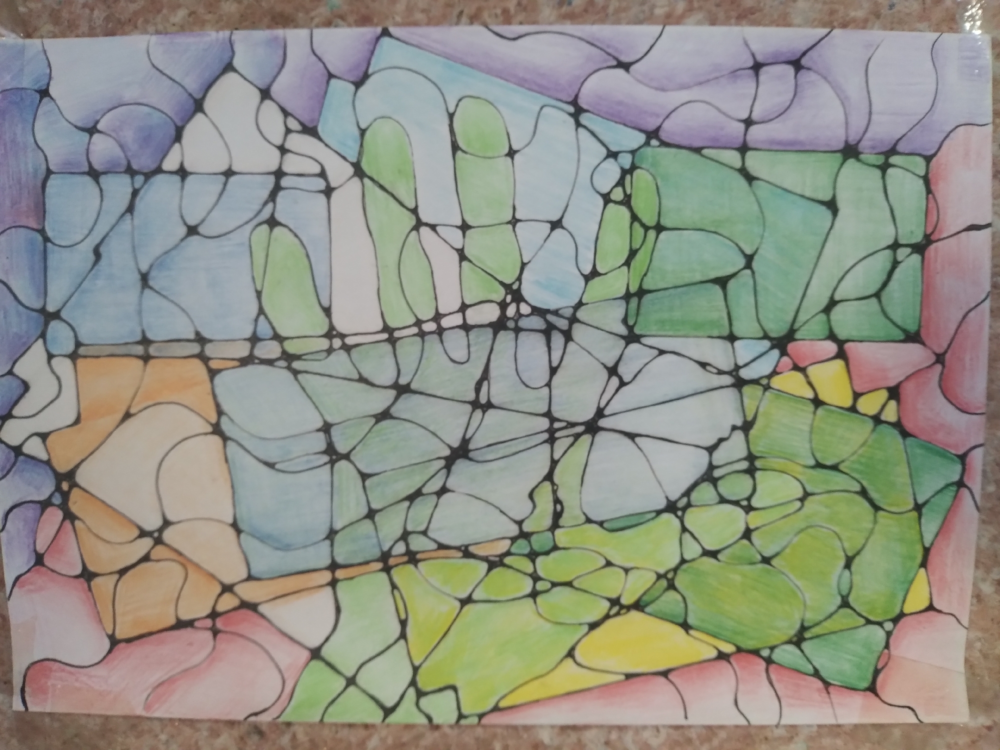 This is a photograph of a piece of abstract art, likely drawn on paper with colored pencils and black ink. The artwork is laid out on a textured, speckled surface that appears to be a countertop or table. The art itself is characterized by a network of irregular shapes outlined in black ink. These shapes are filled with various colors, including purple, blue, green, yellow, orange, and pink. There are no people, animals, or recognizable objects within the artwork. The image does not depict any scene or location in the city of Baki, Uzbekistan, or any other geographical location.