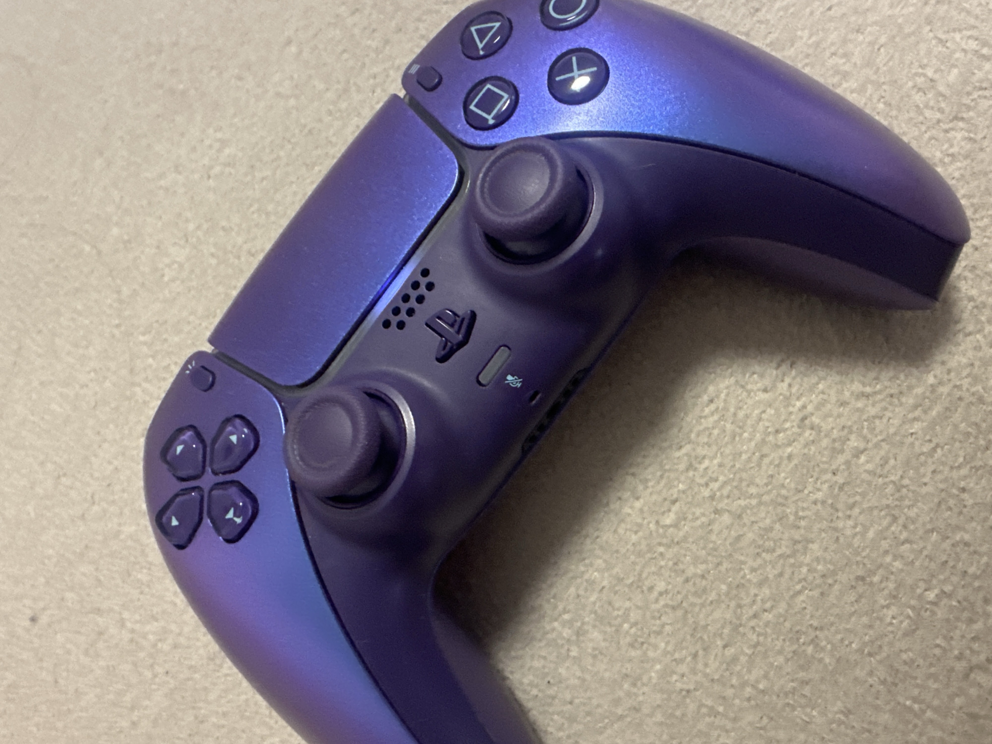 A close-up shot shows a purple PlayStation 5 DualSense controller resting on a textured light grey surface. The controller's buttons and analog sticks are visible, displaying the PlayStation logo and directional arrows. No other objects or people are visible in the frame. The environment is limited to the textured surface beneath the controller. There is no information in this image that indicates a location in Varna, Bulgaria.