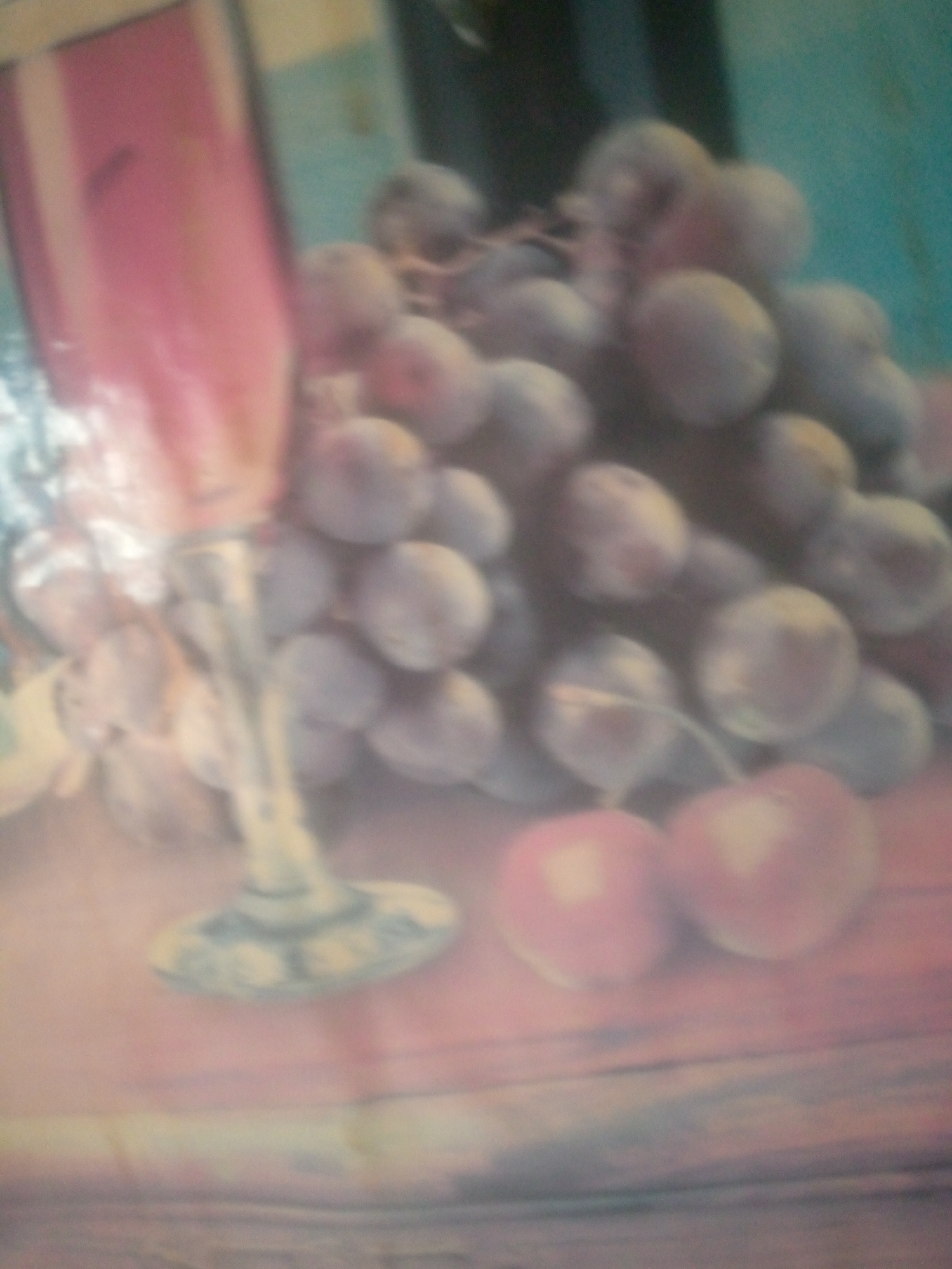 The media file, likely a photograph, displays a still life arrangement of fruits, possibly grapes and cherries, alongside a stemmed glass and a dark bottle, all set on a wooden surface. The overall image is blurry, suggesting a low-resolution capture or intentional soft focus.
The subjects are predominantly fruits. A cluster of dark, round fruits, likely grapes, occupies the central and right portions of the image. They appear to be a deep purple or blue hue. In the foreground, two lighter, rounder fruits, potentially cherries, are visible, their color suggesting a reddish-pink tone. To the left, a tall, slender object with a pinkish tint and a reflective surface is present; this is likely a wine glass. A dark, upright cylindrical object, resembling a bottle, is partially visible in the background, adding depth to the composition. The setting appears to be indoors, with a textured wooden surface serving as the base for the arrangement. The background is a soft, muted teal, providing a gentle contrast to the foreground elements.
There are no visible people or explicit indications of an activity or event taking place; the scene is static and arranged. The lighting is soft and diffused, not indicative of a specific time of day. There are no discernible weather cues, and the location context of Jauro Yinu, Nigeria, does not offer any direct visual cues within the image itself. Emotions are not conveyed as there are no human subjects. No text is visible in the image. The notable details are the blurry nature of the image, the types of fruits, and the presence of a glass and bottle suggesting a possible theme of wine and fruit.