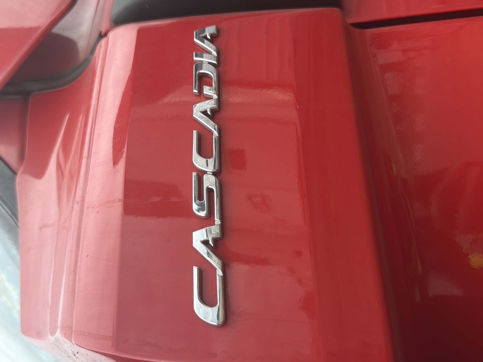 A red vehicle's exterior features the chrome lettering "CASCADIA" on its side. The letters are metallic and reflective, with the word "CASCADIA" clearly legible. The vehicle's surface appears to be clean and well-maintained, with a glossy finish. The background is out of focus, but suggests an outdoor environment, possibly a parking lot or roadside. No people or other objects are discernible in the image. The scene is static and does not depict any action. The location in Murfreesboro, United States of America, is not visually indicated within the image itself.