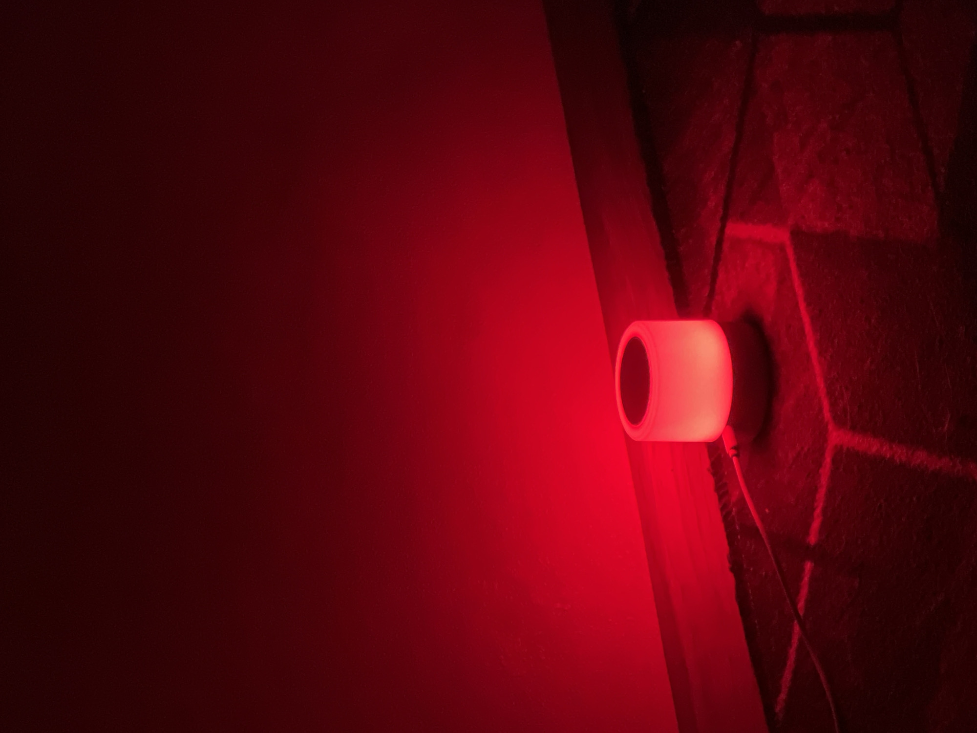 A dimly lit, indoor scene is dominated by a cylindrical object emanating a red light, positioned against a wall with a dark surface or covering. The light casts a strong red glow, illuminating the surrounding area, particularly the wall and the foreground, which appears to be a textured surface, possibly brick or stone. The scene is likely indoors. There are no people present in the image. Without additional information, the specific location in Saint Petersburg, Russia cannot be determined.