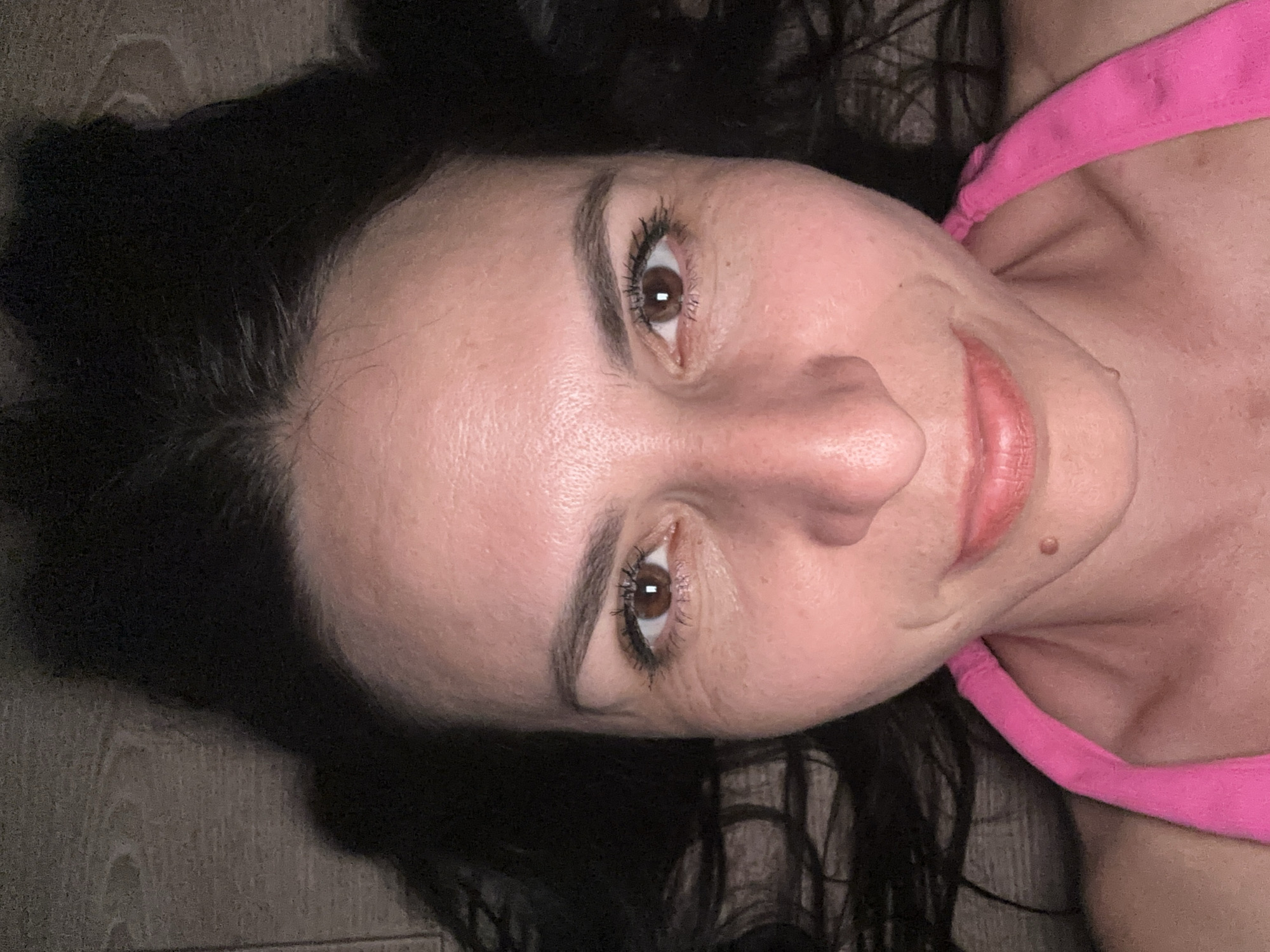 This is a close-up, top-down shot of a woman's face. She has dark hair, brown eyes, and fair skin with some visible freckles and fine lines around her eyes. She is wearing a bright pink top. The background appears to be a wooden surface, possibly a floor. The scene is indoors. There is no identifiable location in Odesa, Ukraine.