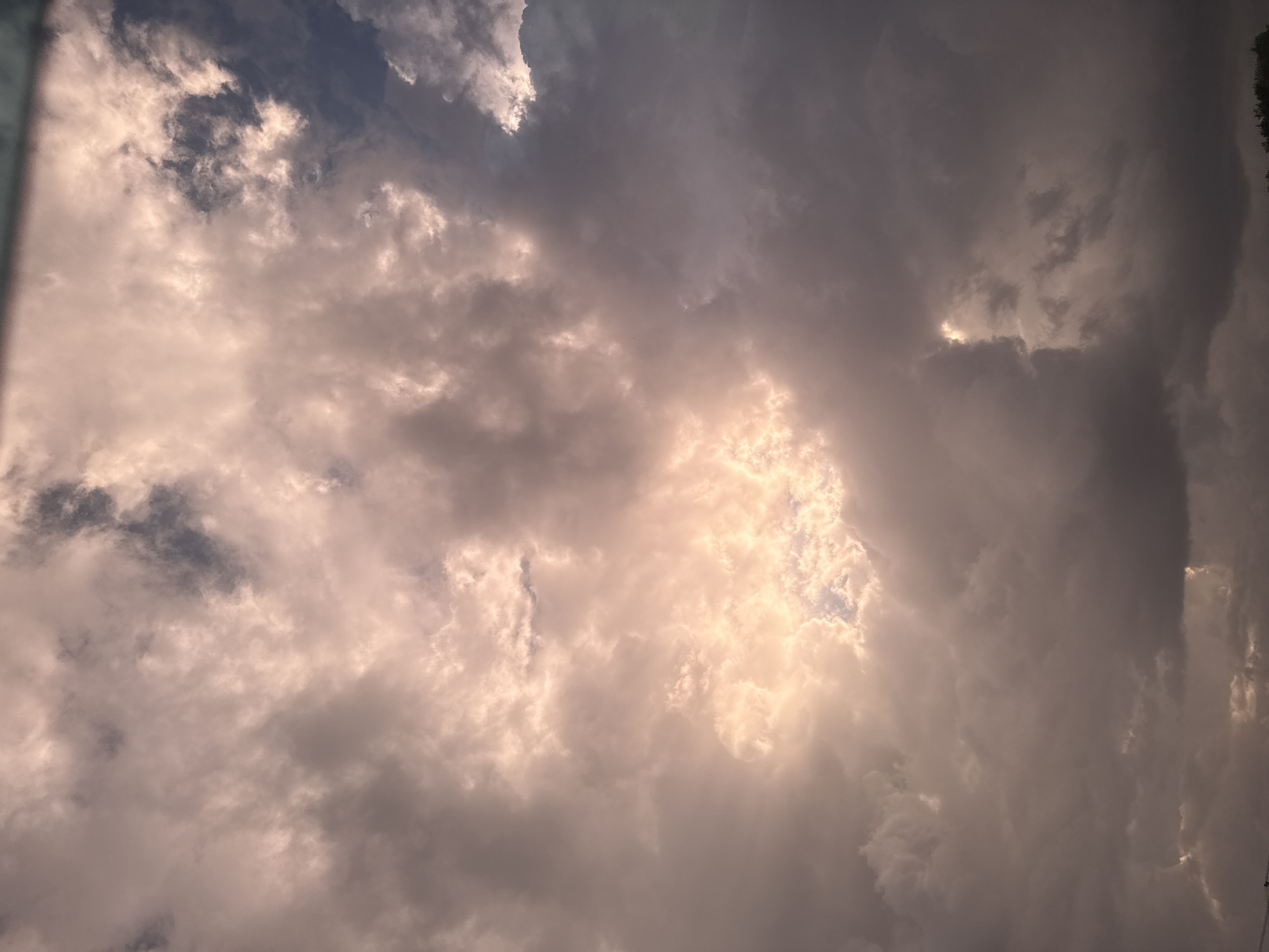 The image shows a sky filled with dramatic, stormy clouds. The clouds are dark and heavy, with patches of bright, warm light breaking through in the center. The light creates a halo-like effect, illuminating some of the smaller clouds within the larger mass. The overall impression is one of a powerful, dynamic weather event. The image does not contain any specific details that would allow for its location to be determined within the city of Berezniki, Russia. There are no people, identifiable landmarks, or any other contextual clues present in the scene. The image is a close-up view of the sky.