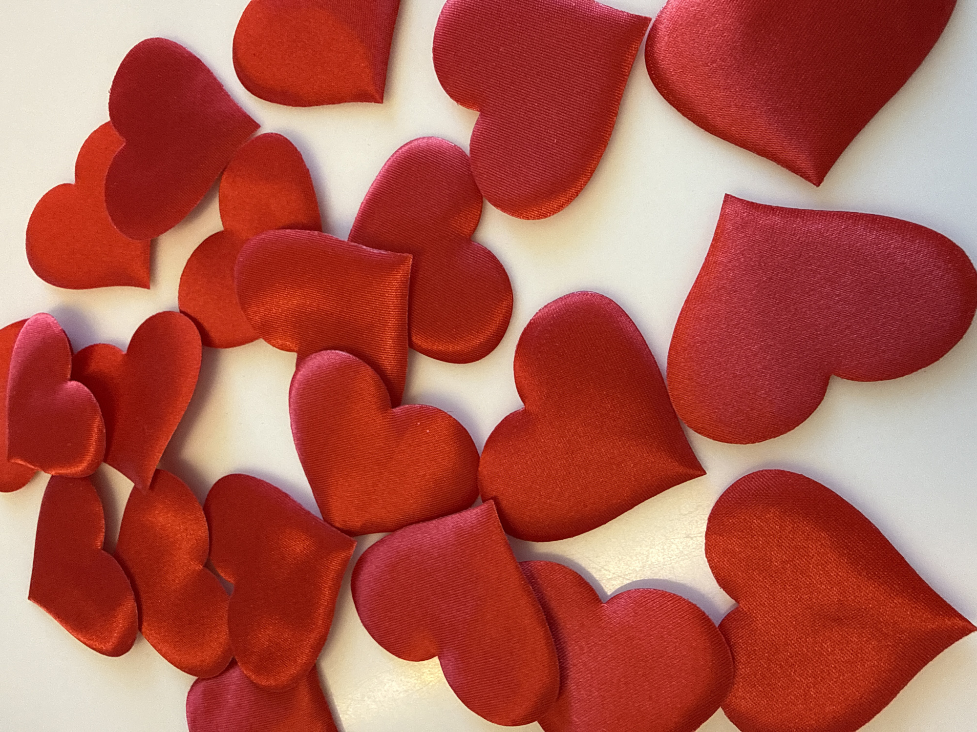 The image displays a collection of red, fabric-covered hearts arranged on a white surface. There is no evidence in the image to indicate a location in Votkinsk, Russia, people, subjects, actions, or interactions. The environment consists solely of the white surface and scattered hearts.