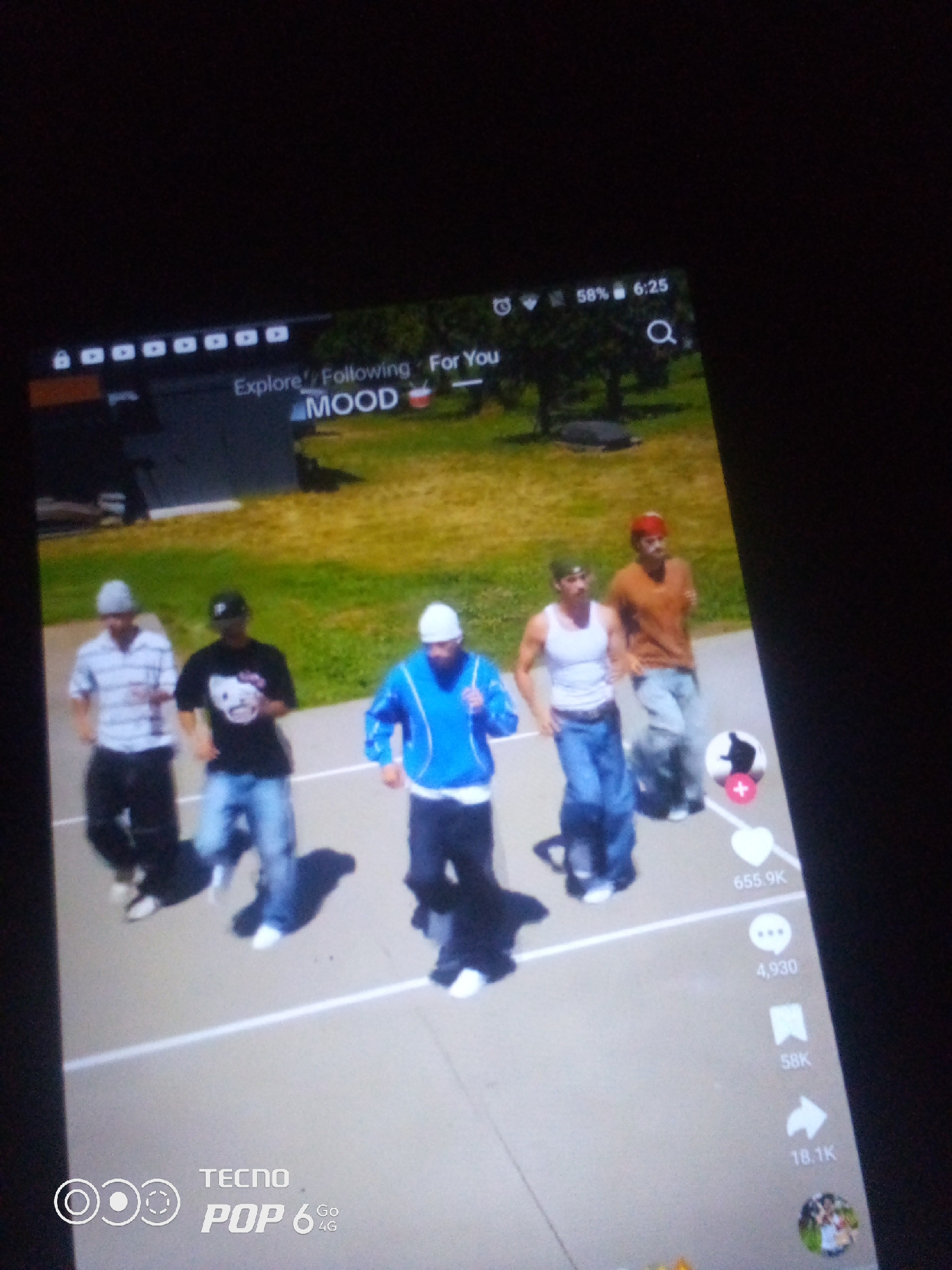 The image shows a screen displaying a video of five young men dancing. The men are dressed in casual clothing, including t-shirts, jeans, and hats. They appear to be on an outdoor court with a grassy area in the background. The screen also displays various social media interface elements, such as likes, comments, shares, and user icons. In the lower left corner, there is a "TECNO POP 6 Go 4G" logo, indicating the device on which the image was captured. The location "Howayi, Nigeria" is not visually represented in the image itself and cannot be determined from the provided visual information.