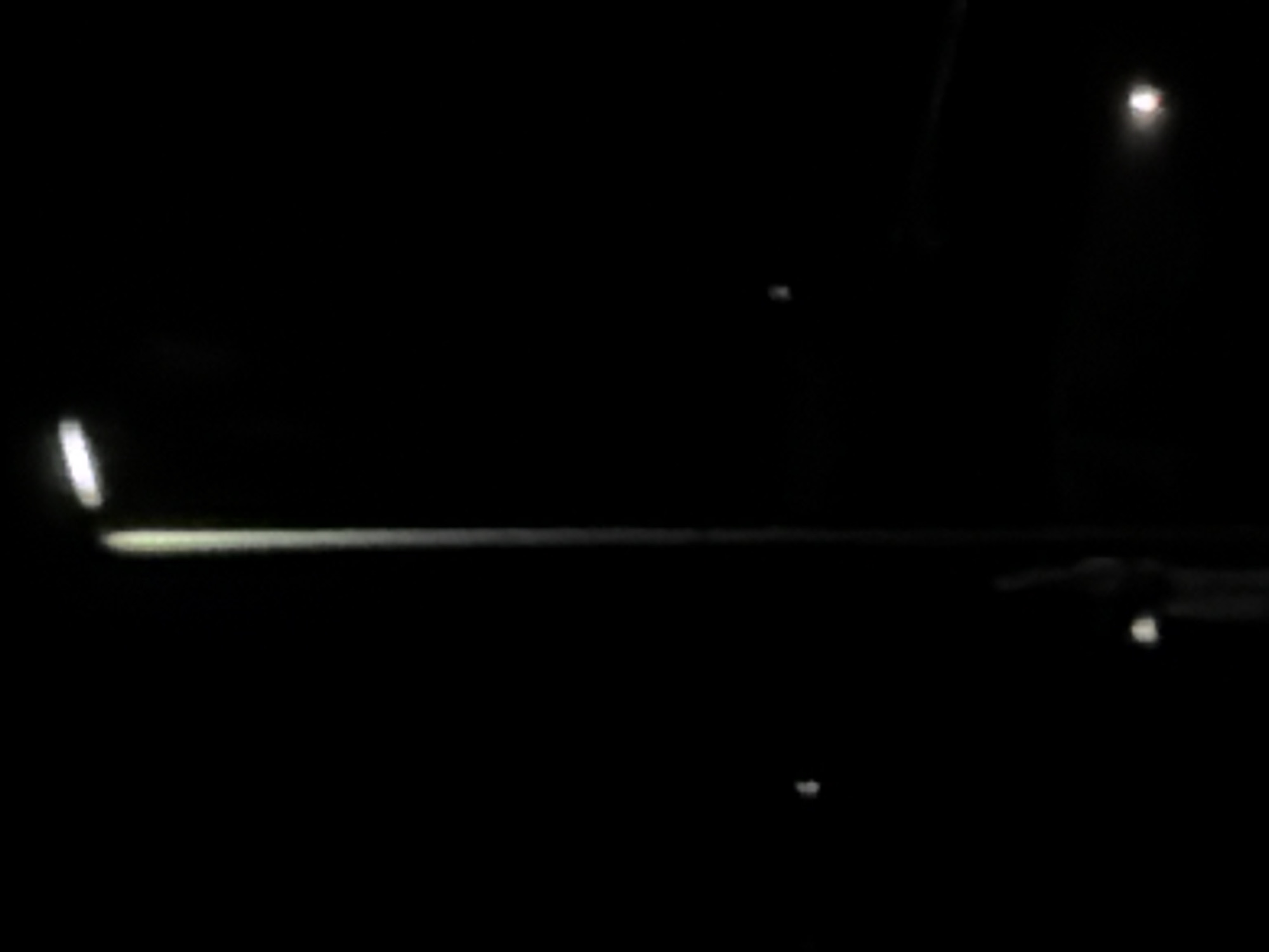 The image appears to be taken at night. A horizontal light source illuminates what may be a road surface or railing. Another light source is visible in the upper right. A darker object is visible in the lower right with a smaller light source underneath. There is no information in the image to verify location in Sant Martí Sarroca, Spain. The lack of detail makes it impossible to identify any people or discern any interactions.
