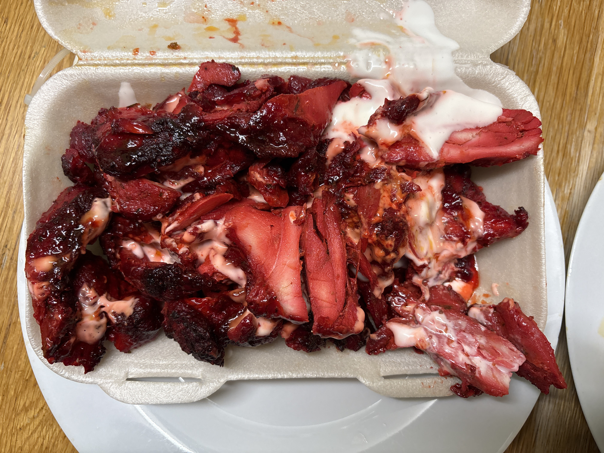 The image shows a styrofoam container filled with char siu pork. The pork is covered in a white sauce. The container is sitting on a wooden surface. The location is Oswestry, United Kingdom.