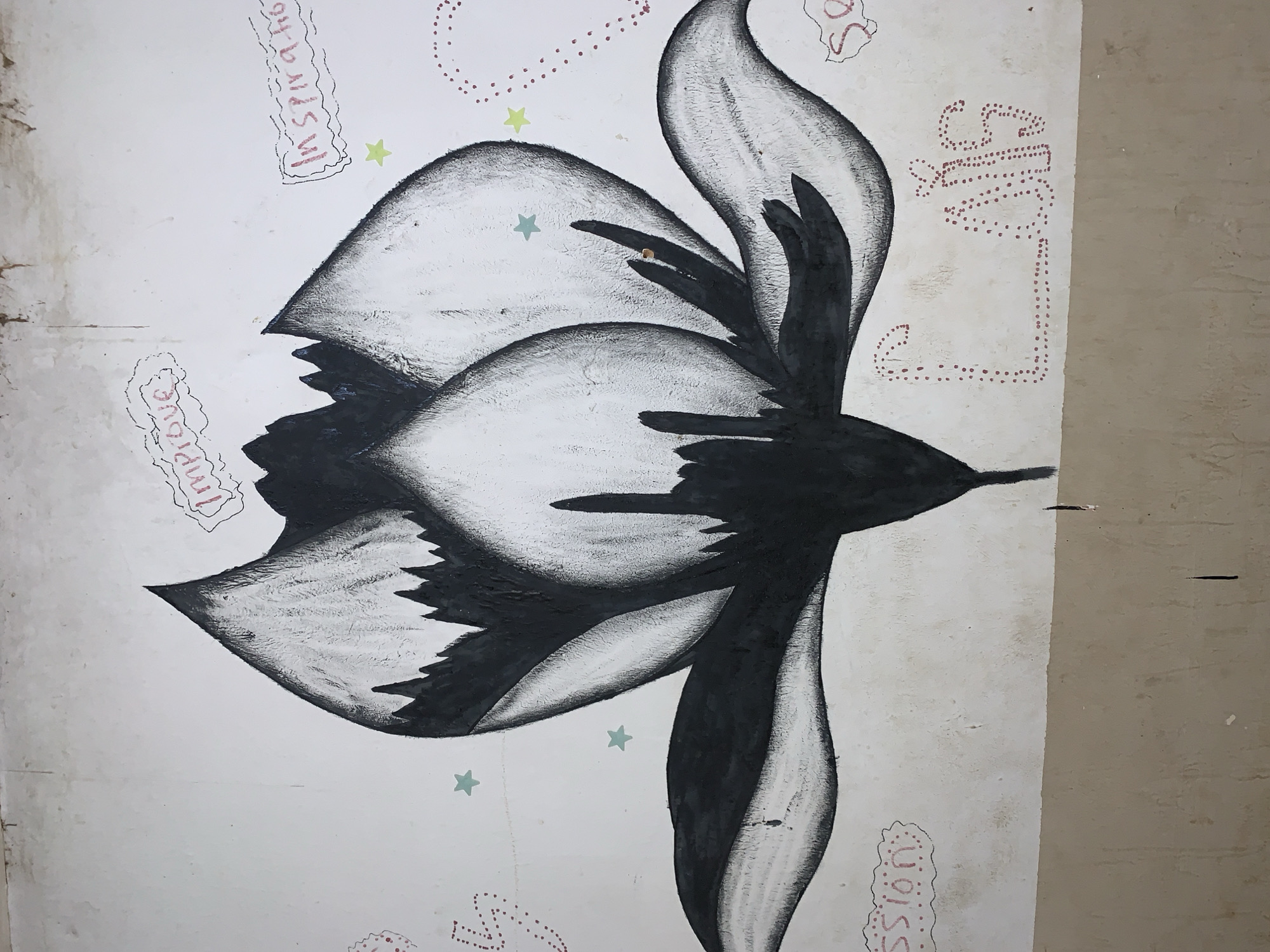 The image depicts a black and white drawing of a flower or bird, featuring curved shapes resembling petals or wings. The artwork is on a wall, with writing like "Inspiration" and "Mission" surrounding the central image. The location is Rafin Par, Nigeria, though that is not verifiable from the image alone.