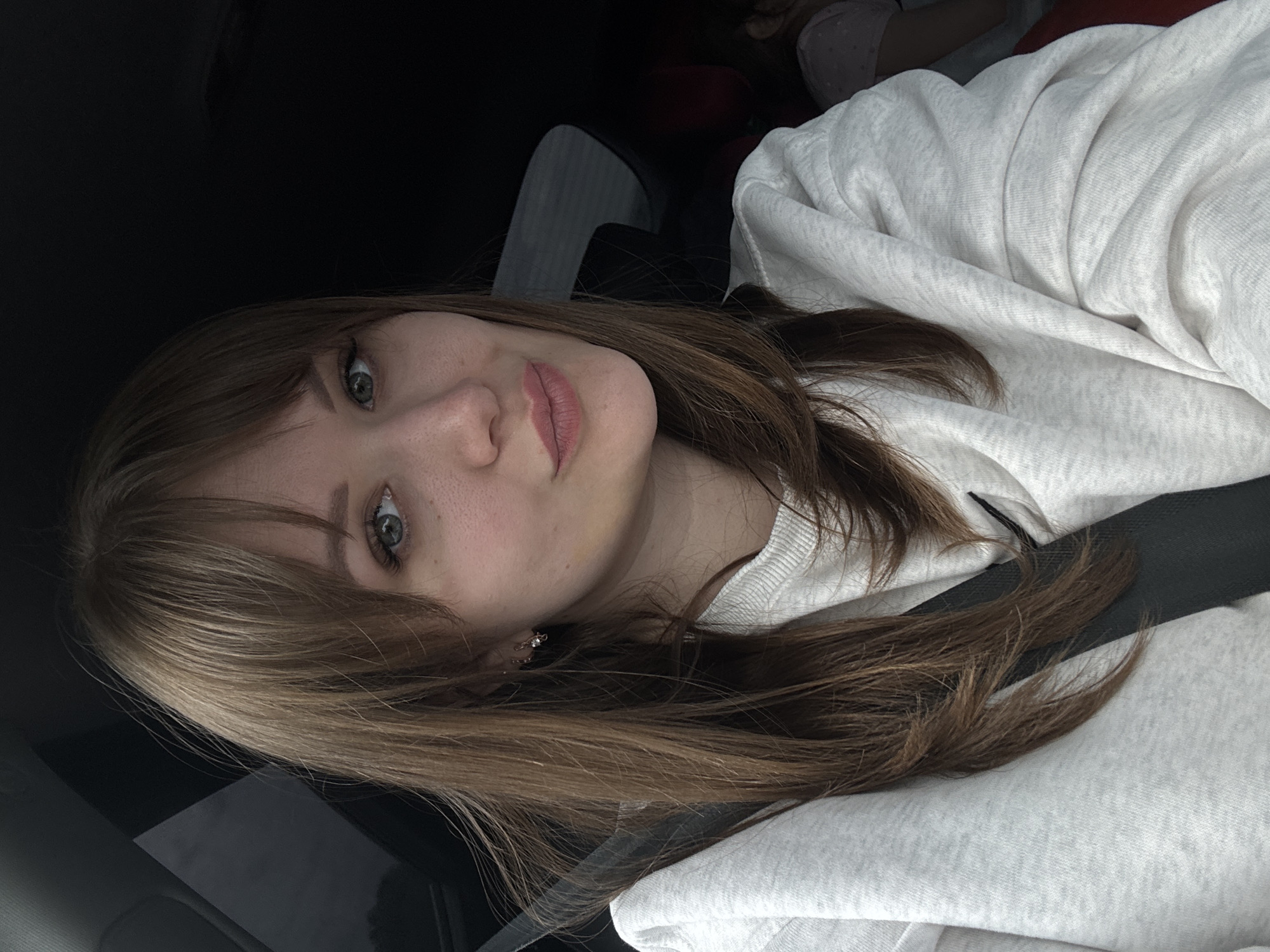 A woman with brown hair and green eyes is wearing a grey hooded sweatshirt. She is wearing a black seatbelt, likely in a car. The background is dark. The location of Ivashevka, Russia cannot be determined from this image.