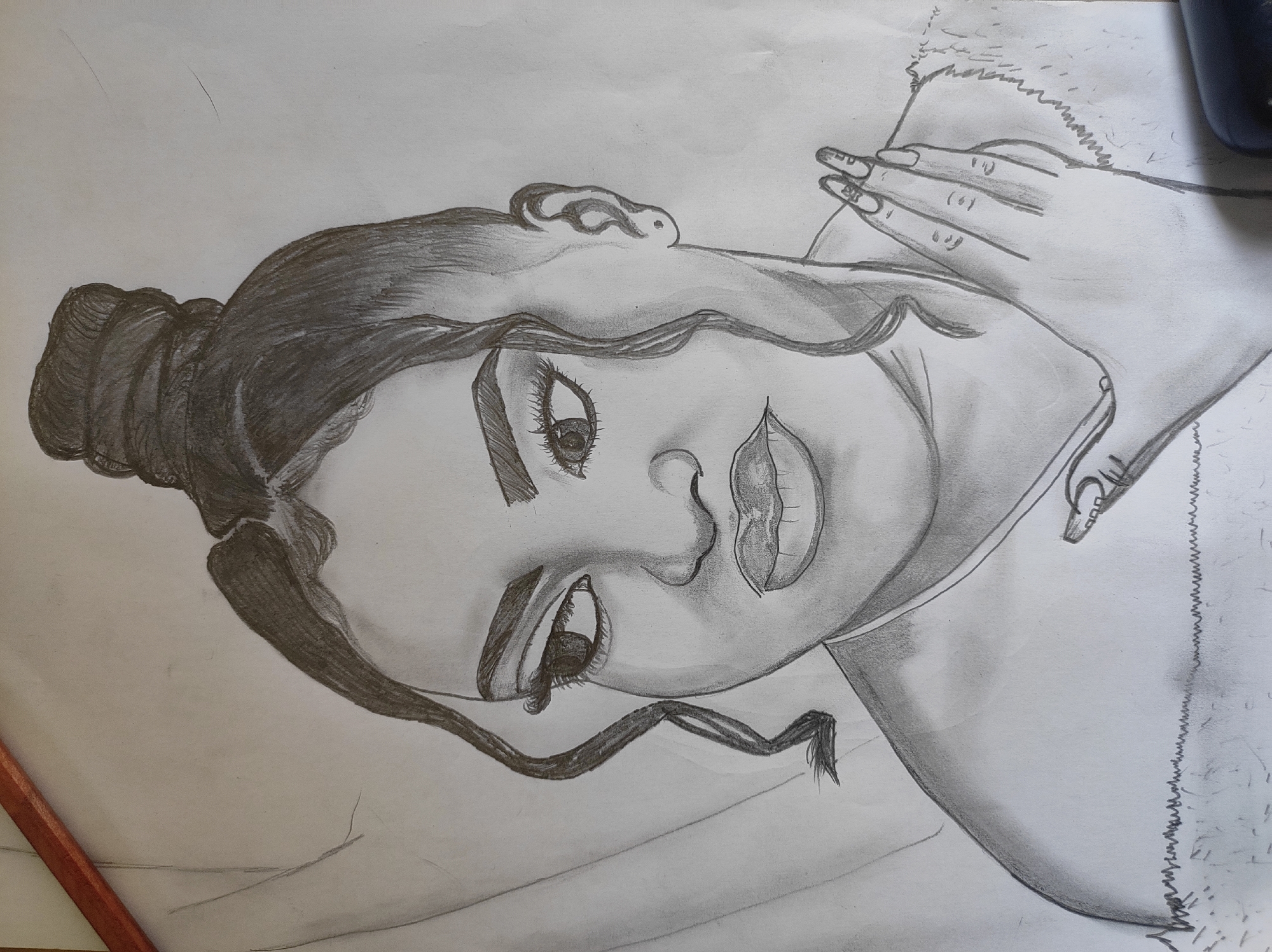 A drawing depicts a woman with a bun hairstyle. She has dark hair, and the drawing includes detailed shading to show contours and light. Her eyes are large and expressive, with distinct eyelashes and eyebrows. Her nose is small, and her lips are full with shading to represent texture and shape. Her hands, with long fingernails, are resting near her neck. The overall drawing style is realistic with a focus on shading and detail to create depth. The background is plain white paper. There is no indication of this image being related to Abuja, Nigeria.