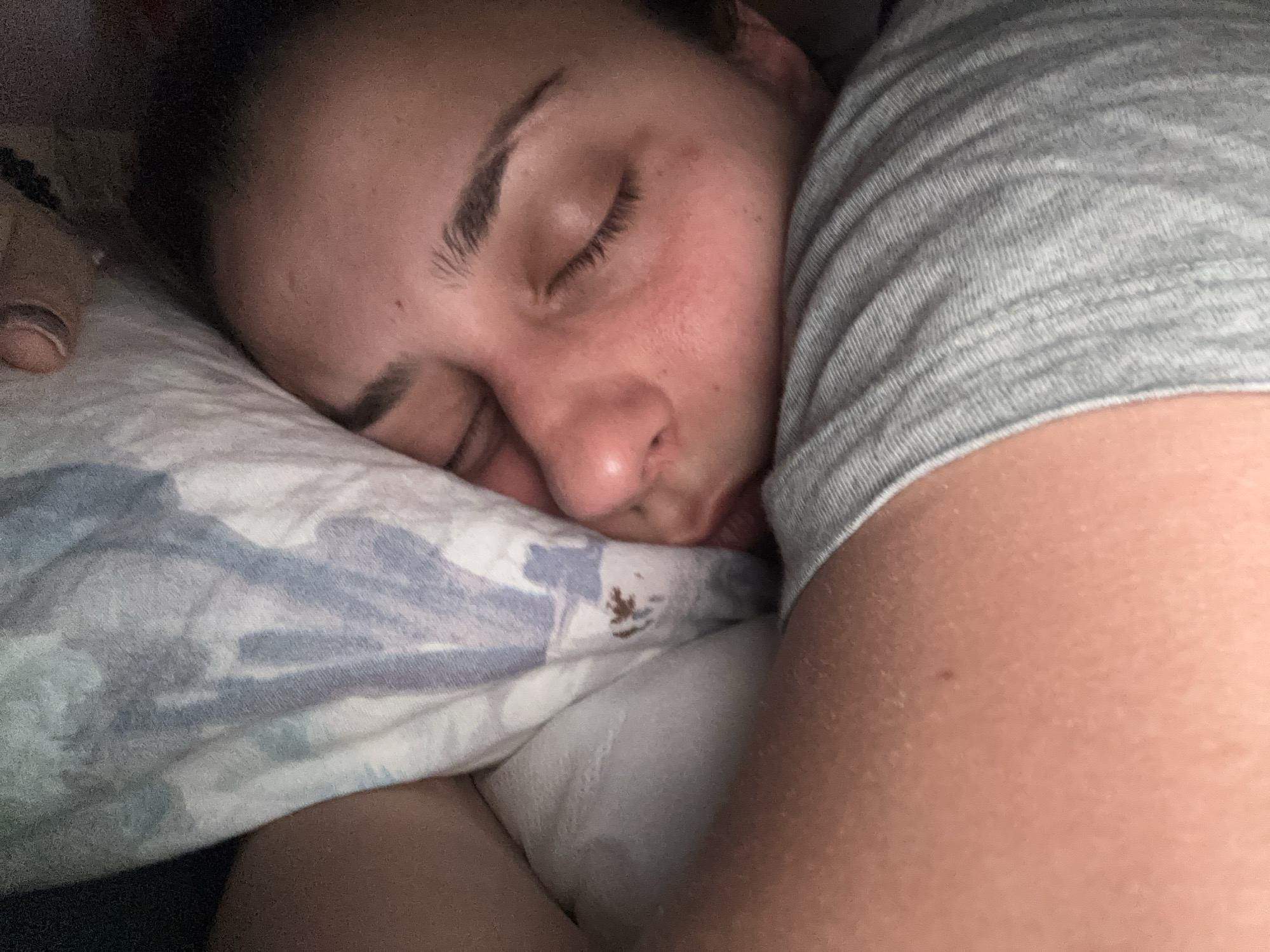 A person is lying on a pillow with their eyes closed, possibly sleeping. The pillow has a blue and white pattern. The person is wearing a gray shirt. The location in the city of Sofia, Bulgaria is not evident in the picture.