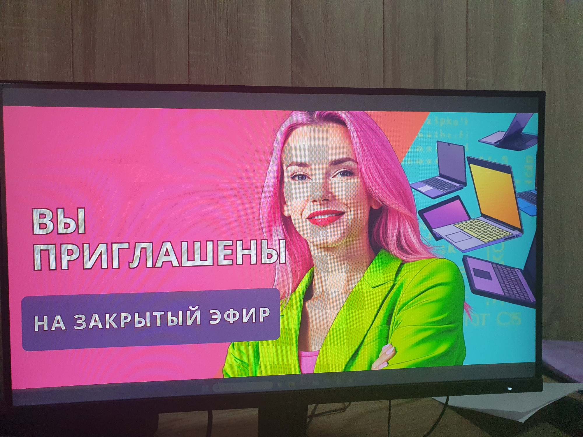The image shows a computer monitor displaying a graphic with a woman with bright pink hair wearing a neon green blazer. The text on the screen is in Russian and reads "ВЫ ПРИГЛАШЕНЫ НА ЗАКРЫТЫЙ ЭФИР", which translates to "YOU ARE INVITED TO A CLOSED BROADCAST". The background of the graphic features stylized laptop icons and what appears to be code. The monitor is placed on a wooden surface. There is no visible indication of the location being Tashkent, Uzbekistan.