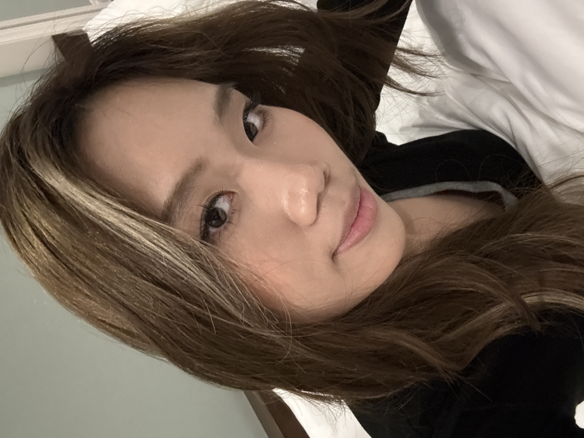 A person is lying on a white pillow in what appears to be a bed. They have light brown hair with highlights. The person is wearing a black top with a gray neckline visible. The background is a light, neutral color, possibly a wall. No details indicate the location of Lanzhou, China, or any city.