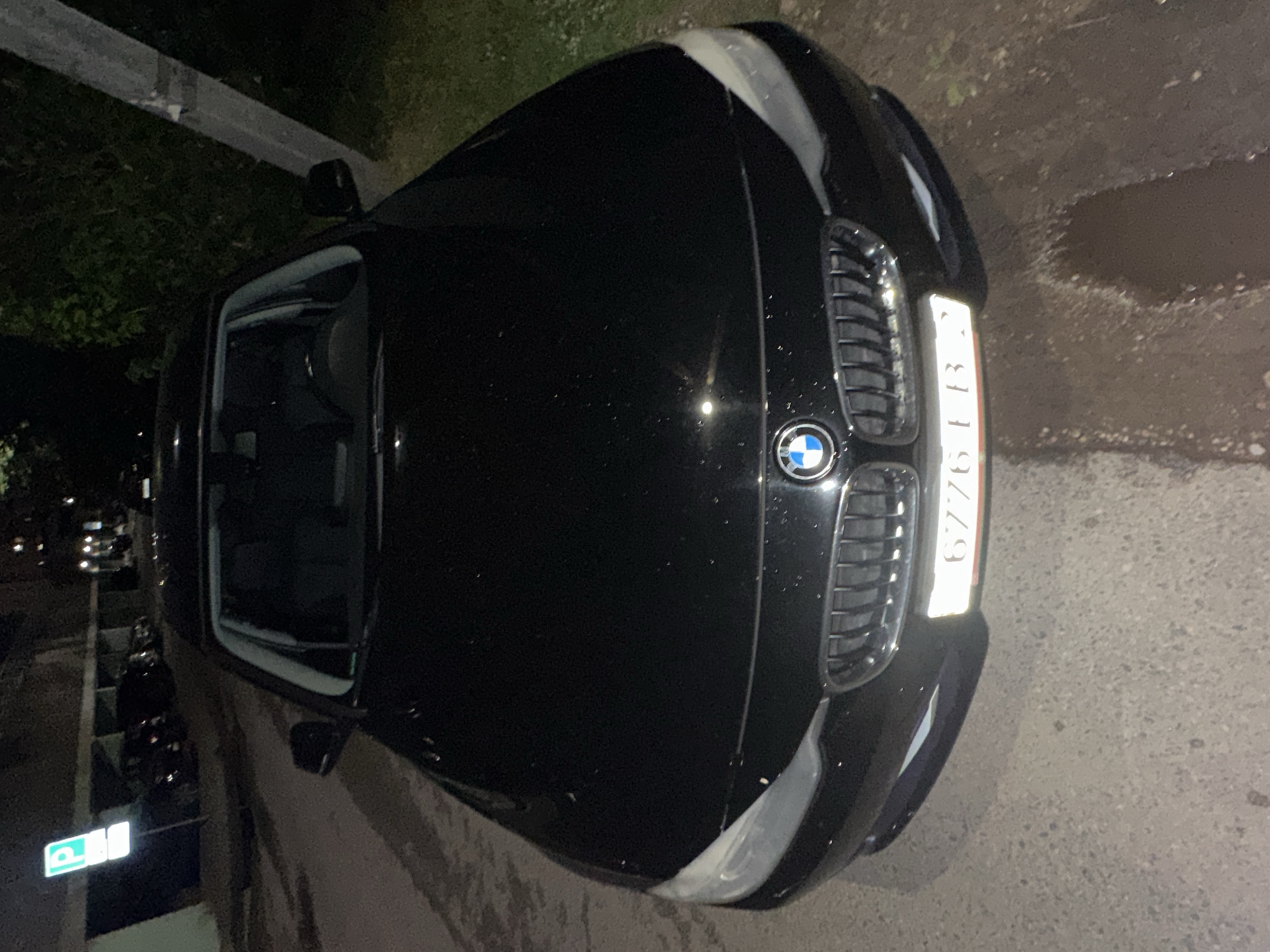 The image shows a black BMW parked in Minsk, Belarus. The car is parked on the side of a street. The license plate number is 6776IB-3.