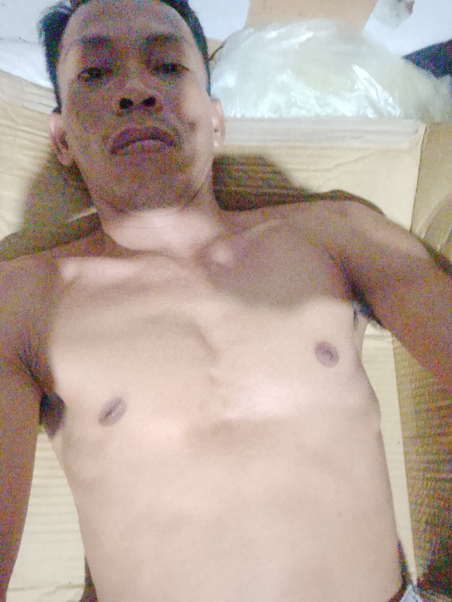 A shirtless man is lying on what appears to be cardboard in Bukit Ketok, Indonesia. A plastic bag is near his head.