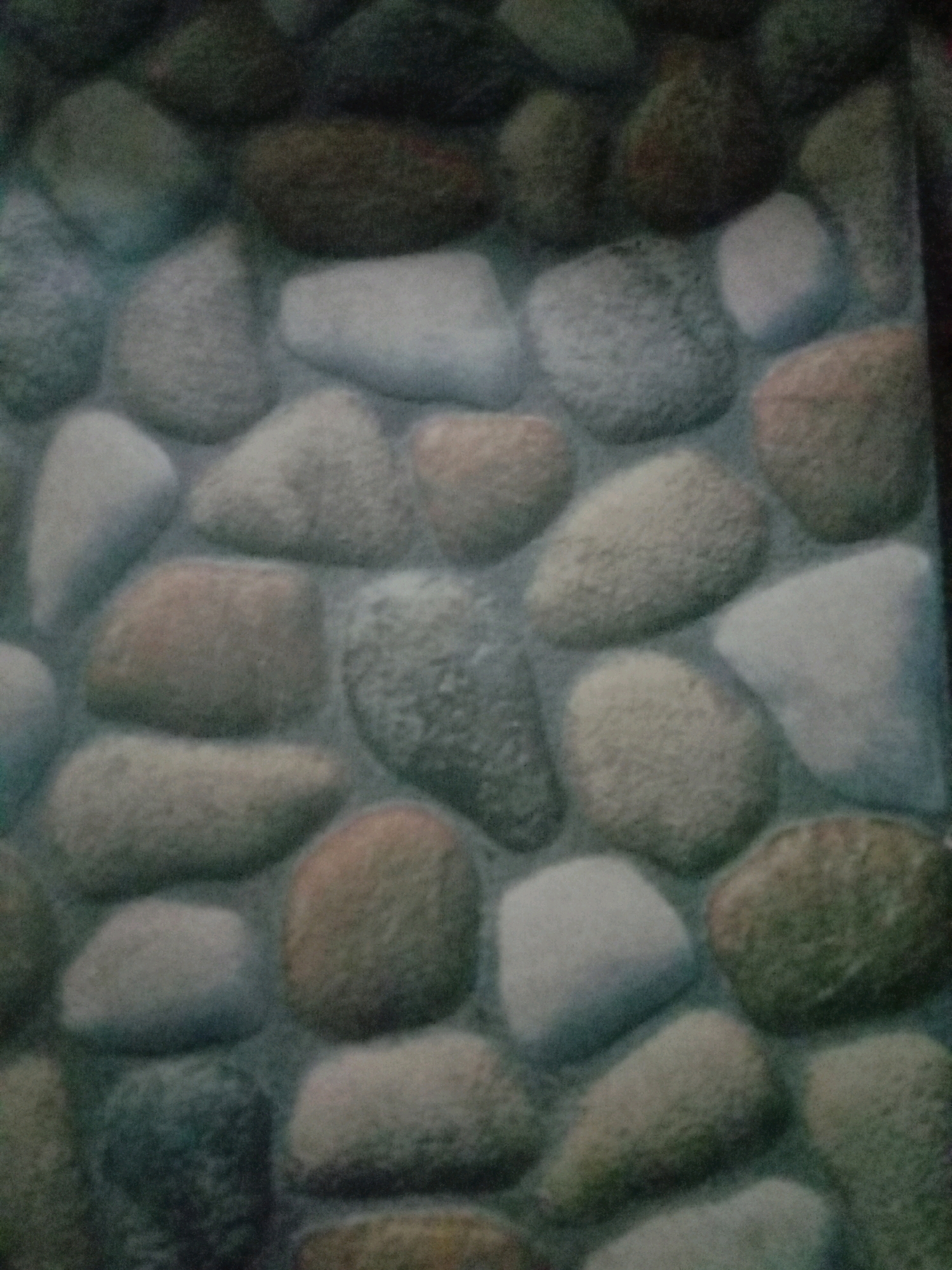 The image shows a close-up of a wall made of various-sized, rounded stones. The stones vary in color, including shades of gray, brown, and white, and are fitted together with a darker grout. The overall impression is that of a natural stone wall. There is no discernible location in the city of Rejosari Mataram, Indonesia, present in the image. There are no people, animals, or specific objects depicted. The scene is static and focuses solely on the texture and pattern of the stonework.