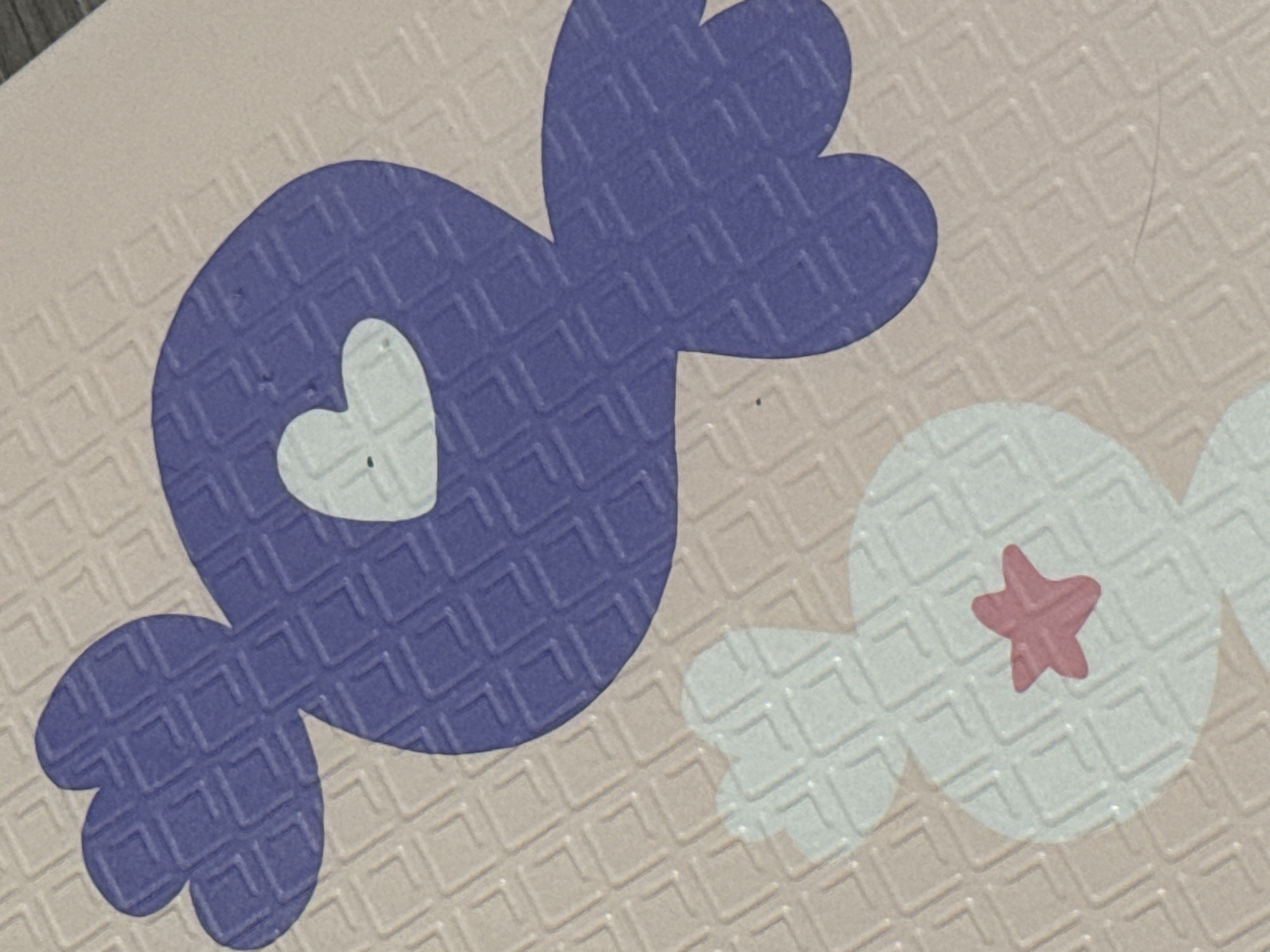 The image shows a close-up of two cartoon-like candy shapes on a textured surface. The candy on the left is purple with a white heart in the center. The candy on the right is white with a pink star in the center. The textured surface has a repeating grid pattern. The location is Unknown, Unknown.