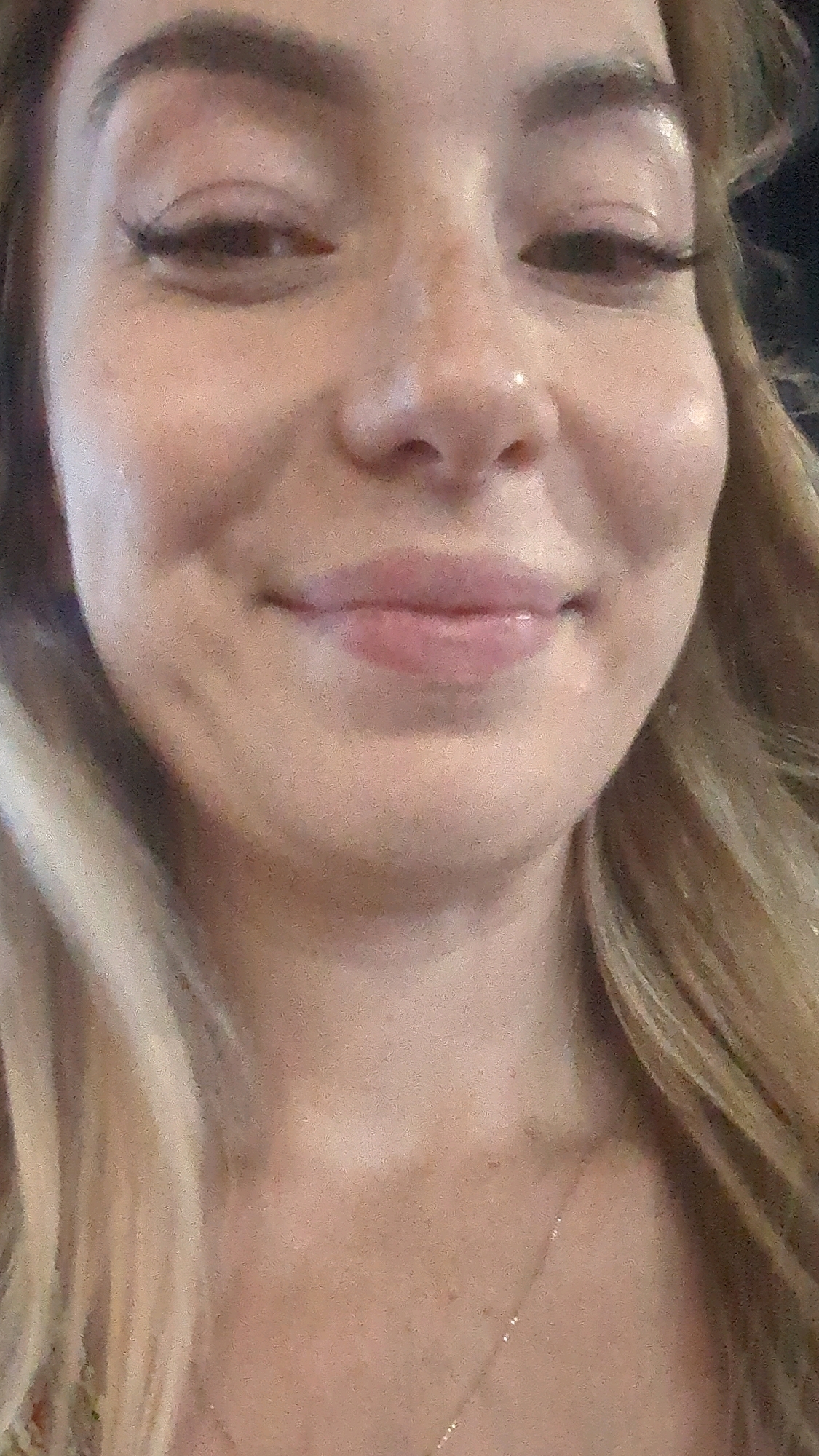 This is a close-up, waist-up photograph of a young Caucasian woman with blonde hair and fair skin. She is looking directly at the camera and appears to be smiling slightly. She is wearing makeup, including eyeliner and lipstick. There is a fine, gold necklace visible on her décolletage. The background is dark and out of focus, suggesting an indoor or evening setting. There is no discernible indication of a specific location in the city of Chișinău, Moldova.