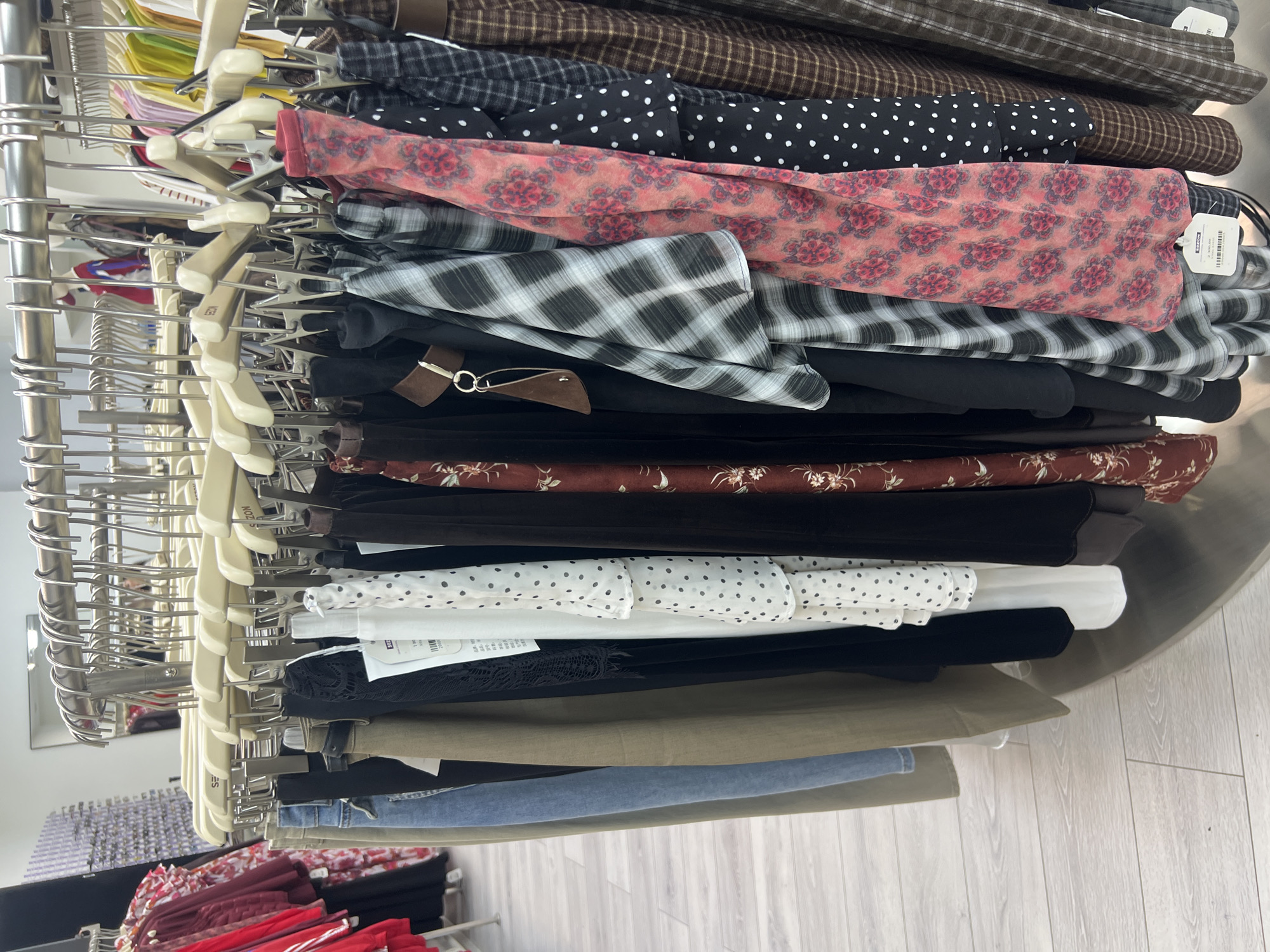 This image depicts a rack of women's clothing in what appears to be a retail store. The clothing items are hung on hangers and include skirts and possibly dresses, with various patterns such as polka dots, plaid, and floral prints. The overall impression is of a boutique or a section of a larger clothing store. The scene does not provide any specific visual cues to pinpoint its exact location within Osh City, Kyrgyzstan.