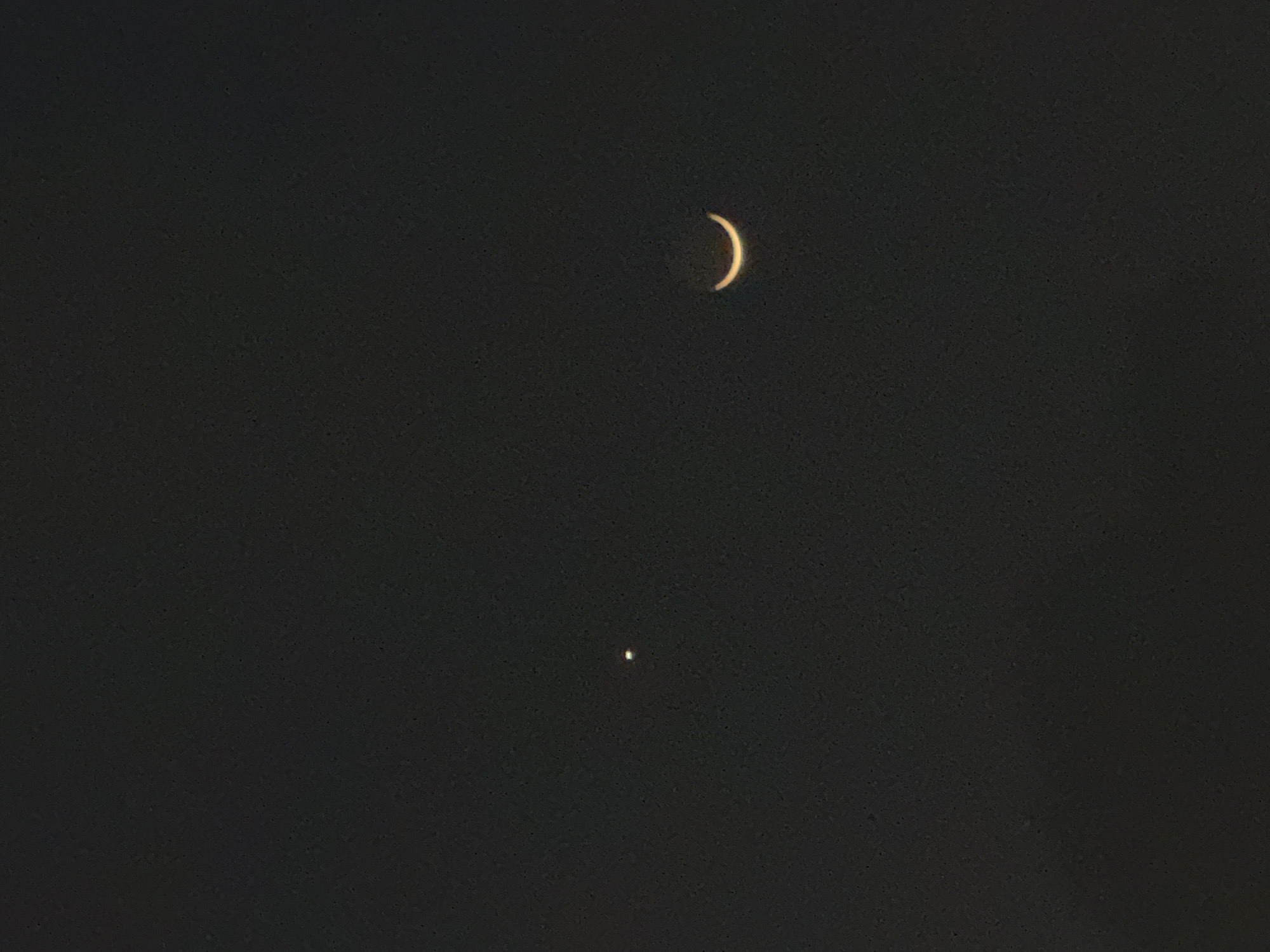A crescent moon is visible in the dark sky over Puebla, Mexico. Below the moon is a bright, point-like object, likely a planet or star. The overall scene is dark, suggesting a nighttime environment.