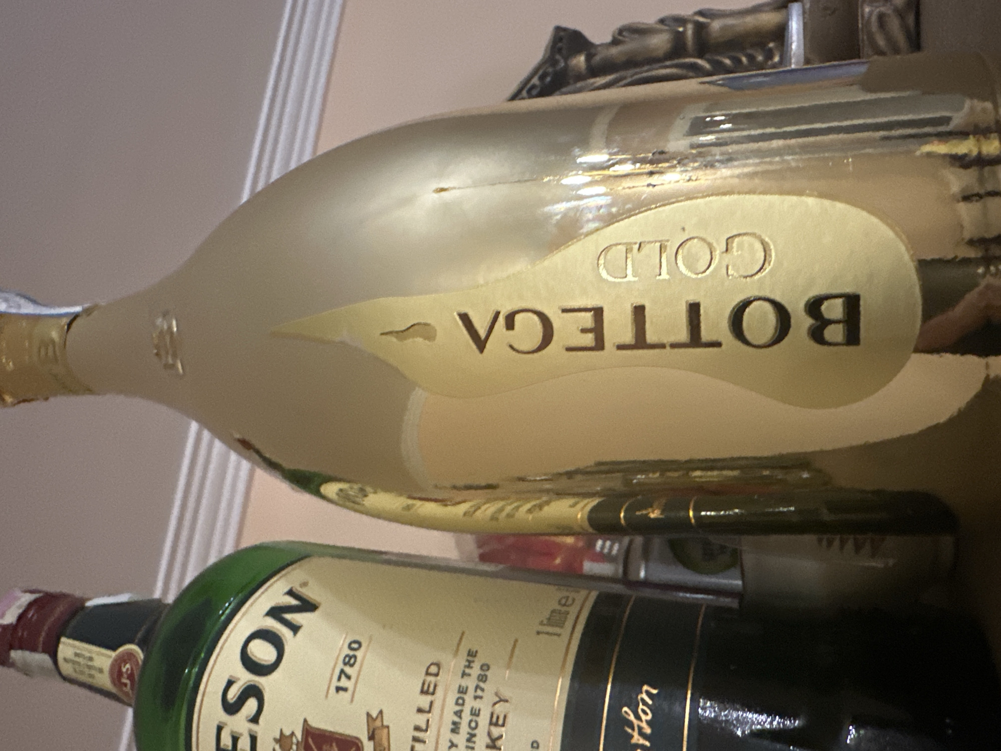 The image shows two bottles of alcohol. The top bottle is a gold-colored bottle labeled "BOTTEGA GOLD". The bottom bottle is green and labeled "JAMESON 1780".