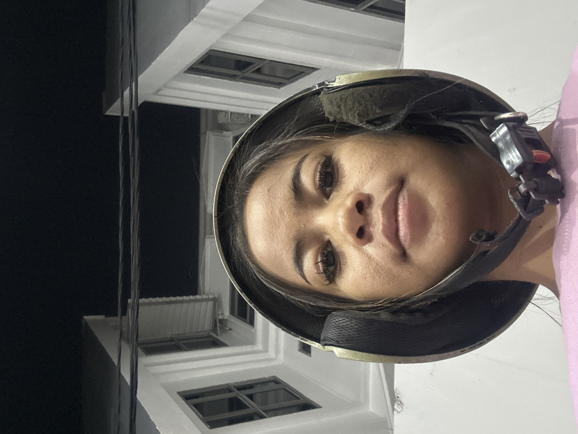 A woman wearing a helmet faces the camera. The background shows a building with windows, suggesting an urban environment. The location is Central Jakarta, Indonesia.