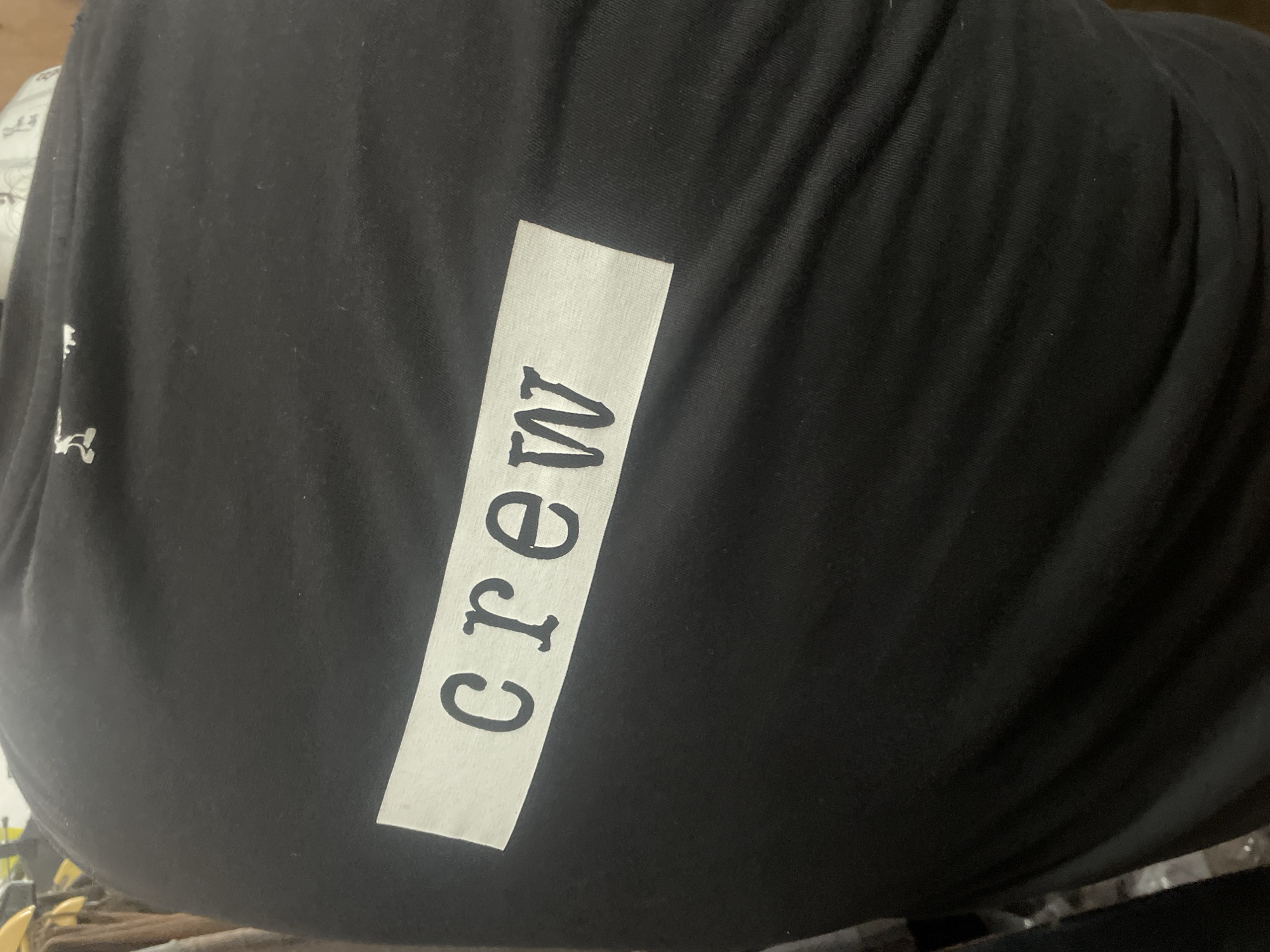 A black garment with the word "crew" printed vertically on a white patch is prominently displayed. The fabric of the garment appears to have some folds or creases. The surroundings are somewhat indistinct, with hints of objects in the background, but the focus remains primarily on the black garment with the "crew" insignia. The location and details about Mumbai, India, cannot be determined from the image.