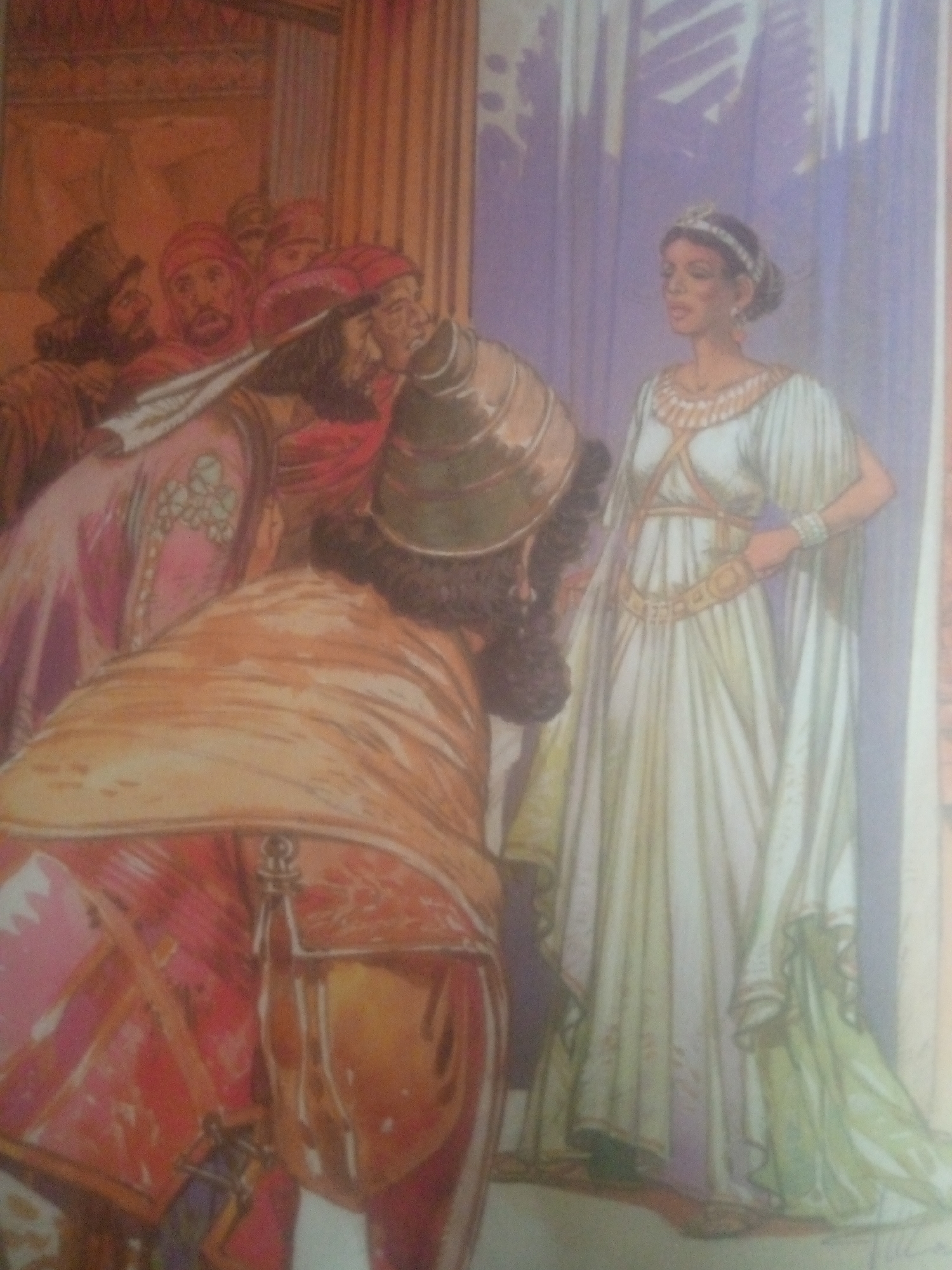 The image depicts an interior scene with multiple figures dressed in historical or fantastical attire. On the right, a woman in a long, flowing white gown with gold trim and a tiara stands looking to her left. Her arms are akimbo. To her left, and partially obscuring her, is a figure in a large, ornate orange and red garment with a distinctive helmet or headdress. This figure is facing away from the viewer. In the background, several other figures, mostly men, are clustered together, wearing turbans and similar historical clothing. The setting appears to be indoors, possibly a palace or temple, with decorative columns or drapery visible. There is no indication of the city of Jauro Yinu, Nigeria.