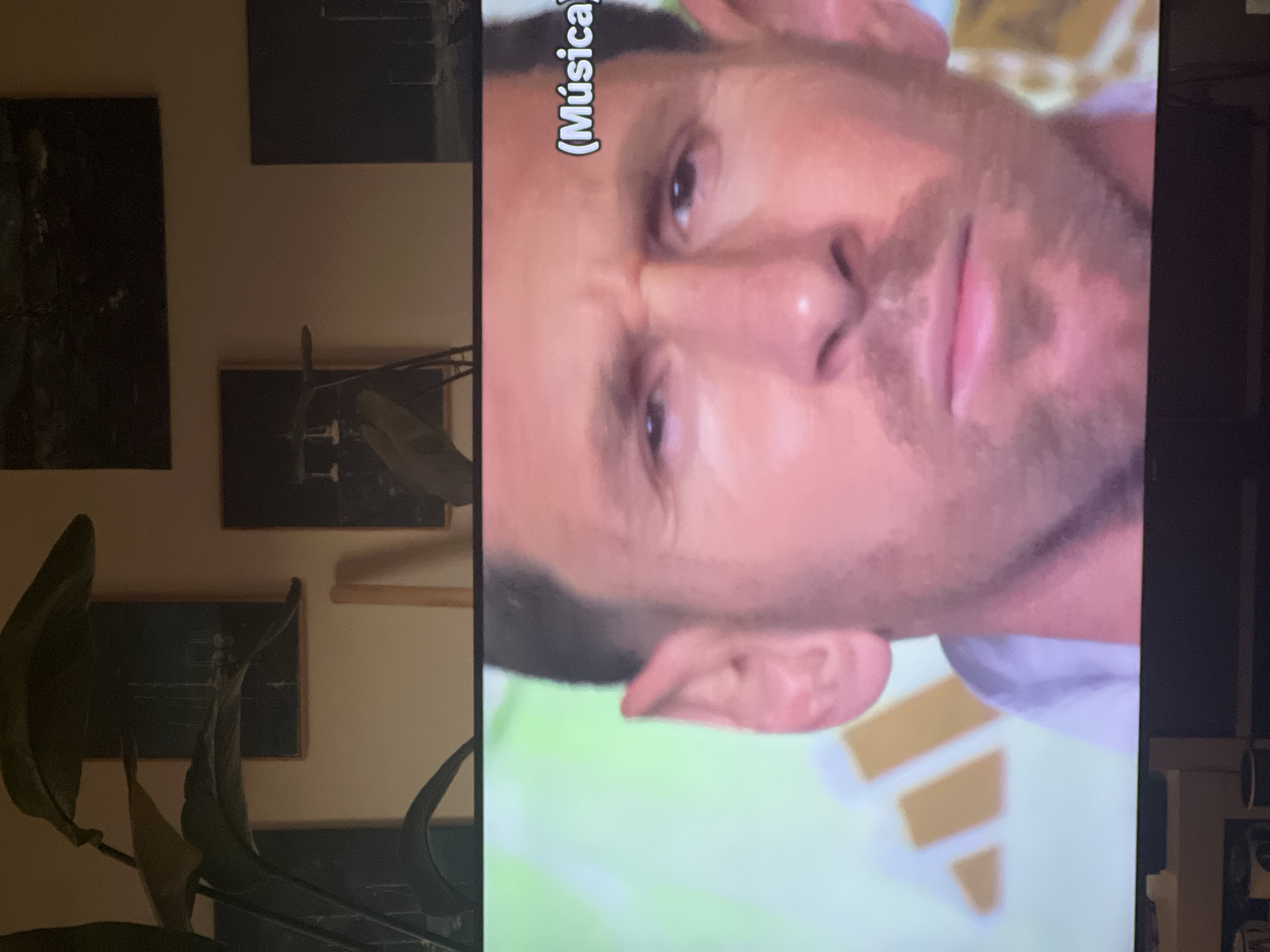 The image is a close-up of a man's face, likely a television broadcast, with a subtle green background featuring an Adidas logo. The man has fair skin, dark hair, and is wearing a light-colored shirt. His expression is serious, with furrowed brows and a neutral mouth. Text overlays the image, indicating "(Música)" in the upper right corner. The background of the scene shows framed artwork on a wall, suggesting an indoor setting. The image does not contain enough information to determine its location in Mollet del Vallès, Spain.
