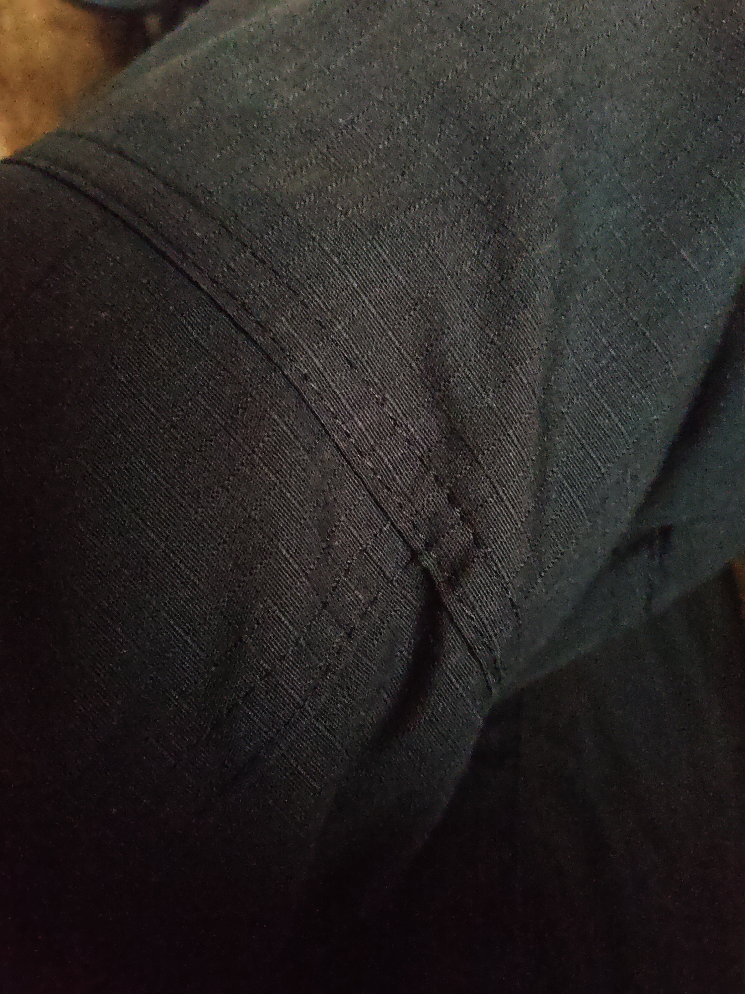 The image shows a close-up view of dark, textured fabric, possibly denim or canvas, with visible stitching creating seams and folds. The fabric has a diagonal weave pattern. There are no people, actions, or interactions depicted. The environment is not discernible. The location of Platoshino, Russia, is not relevant to the visual content of this image.