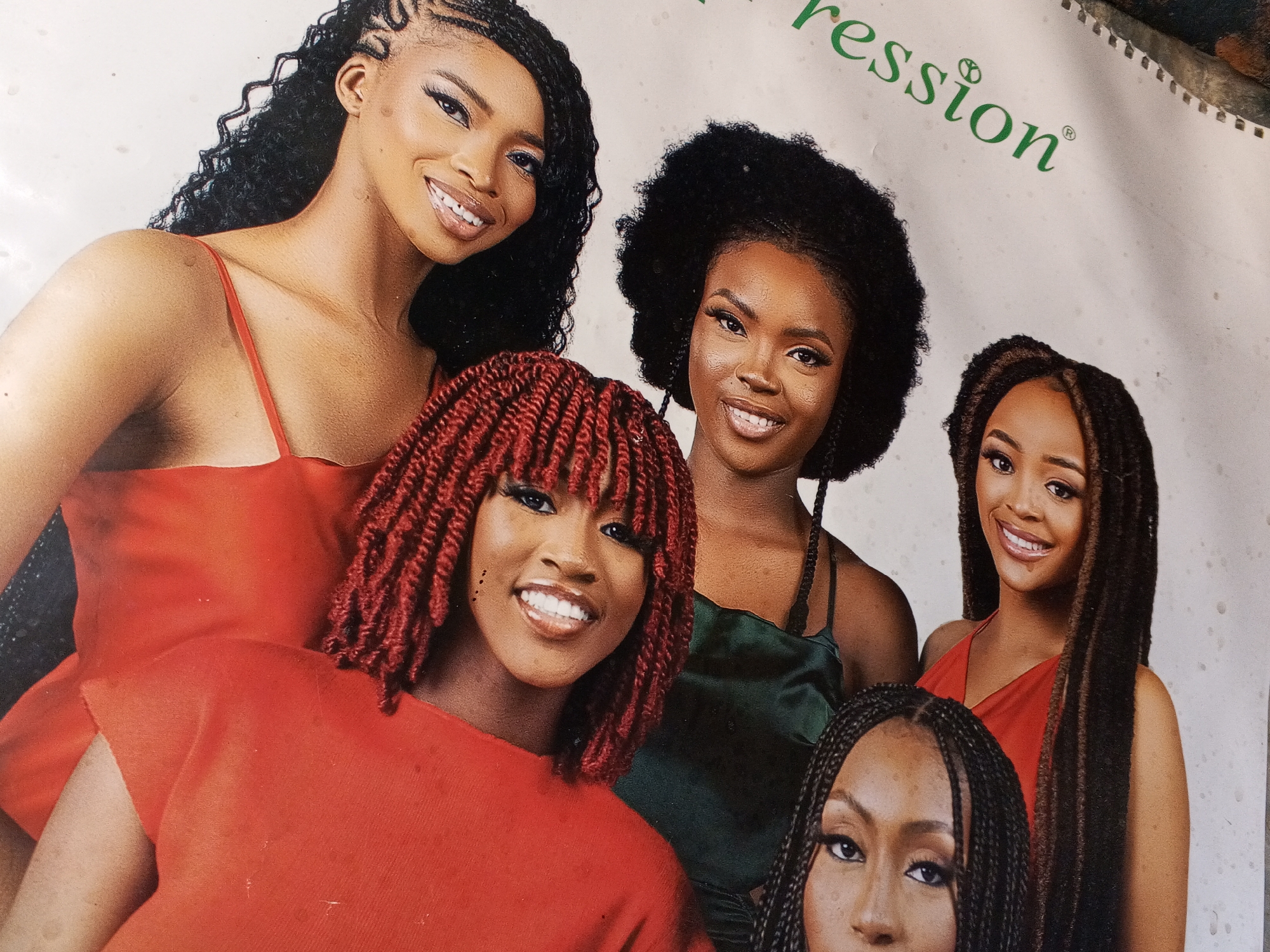 The image is a close-up of a promotional poster featuring five Black women with various braided and styled hairstyles. The women are wearing different colored tops: red, green, and black. They are all smiling. "Expression" is printed in green in the upper right corner. The poster is likely for a hair product or salon. The location in Gwong, Nigeria is not evident from the image.