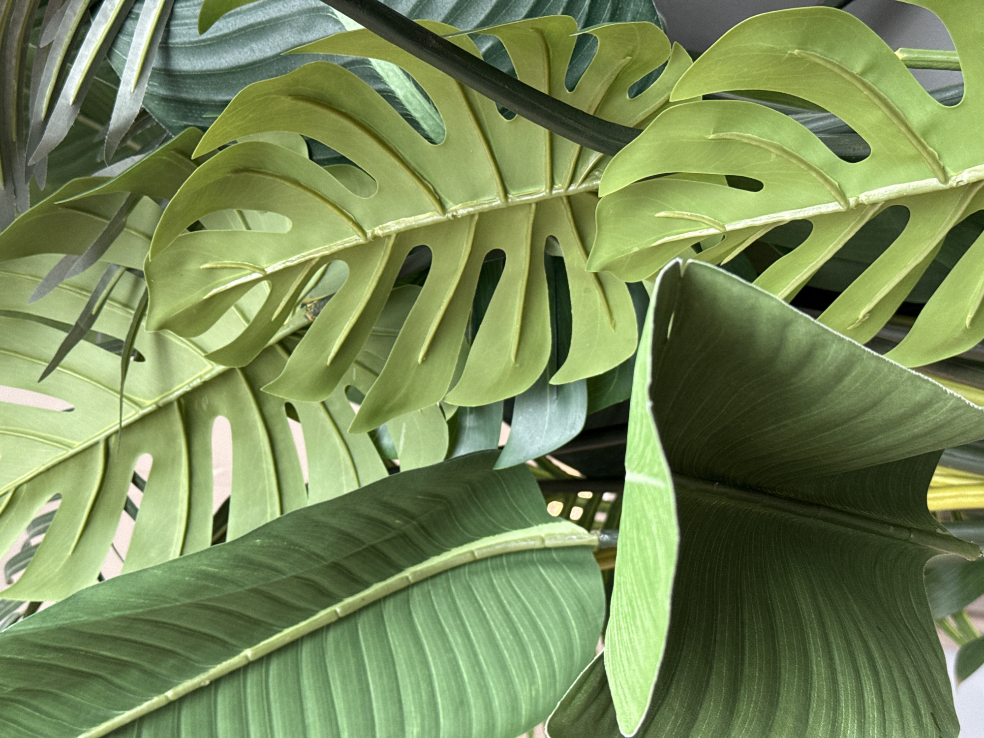 The image shows a close-up view of several large, green artificial leaves, including monstera and banana leaves. The leaves are densely packed together, creating a lush, tropical aesthetic. No people or specific location are discernible from the image, so I cannot confirm it is in Votkinsk, Russia.