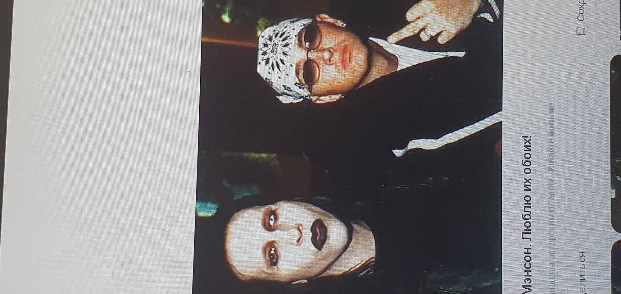 The image shows a close-up, full-body photograph of two men. The man on the left, identified as Marilyn Manson, has pale skin, dark lipstick, and dark eye makeup. He is wearing a dark, long-sleeved shirt. The man on the right, who appears to be Eminem, is wearing a white bandana with a black pattern, sunglasses, and a black jacket over a white t-shirt. He is making a gesture with his right hand, showing his middle finger. The background is dark and appears to be an indoor setting, possibly with some out-of-focus elements that could be a wall or stage. The image is a screenshot from a digital display, as indicated by the text overlay at the bottom of the image, which is in Russian and includes the phrase "Мэнсон. Люблю их обоих!" (Manson. I love them both!). There is no indication of the city of Bat Yam, Israel, or any other specific location in the provided image.