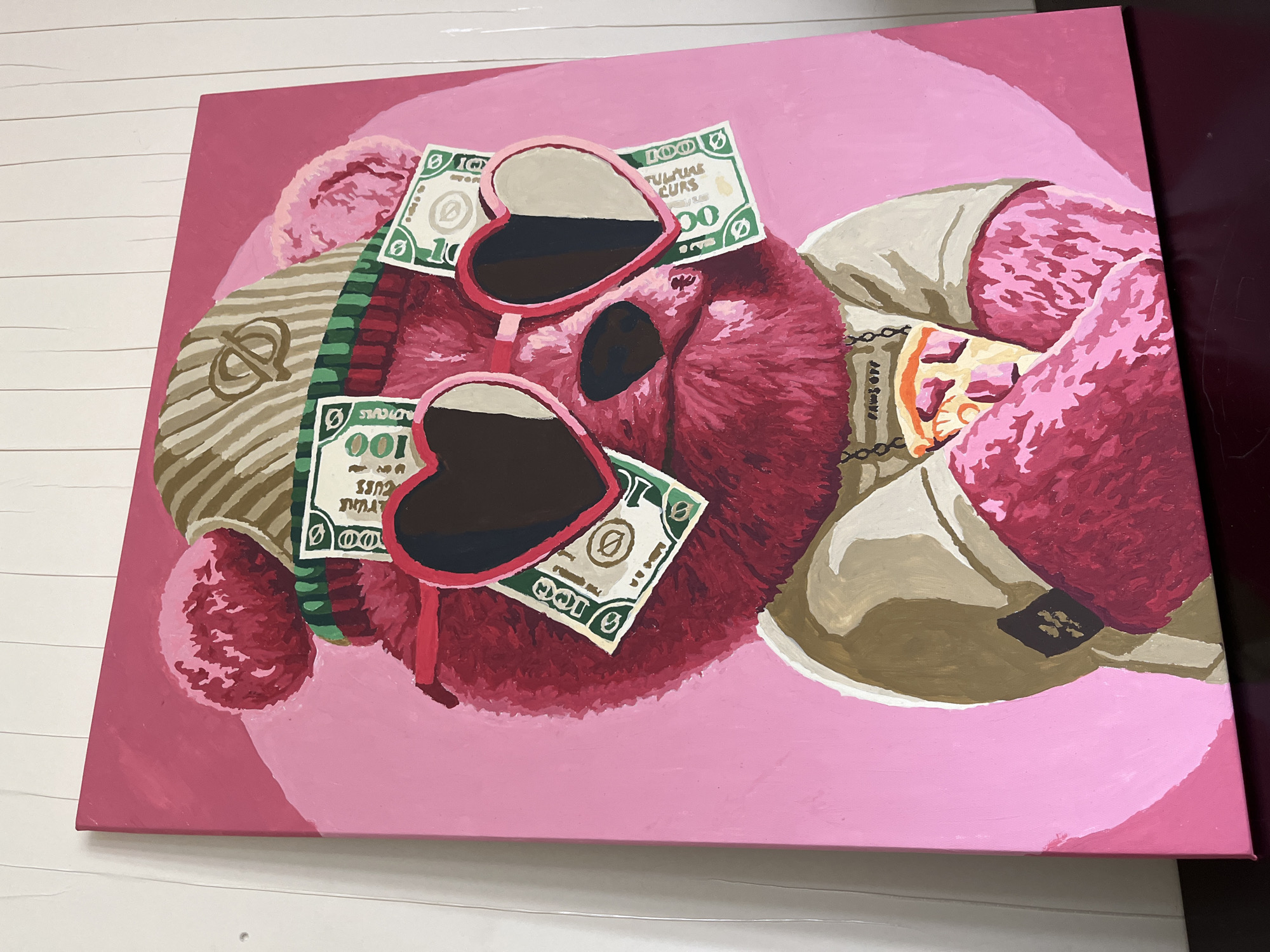Here is a description of the image:
The image is a close-up shot of a rectangular painting on a white surface with a white wall in the background. The painting depicts a pink furry object or character with heart-shaped sunglasses resting on its face. Scattered around the character are several US dollar bills. The character also wears a designer scarf and sits on top of a designer bag. The background of the painting is a solid, lighter shade of pink. The overall style is cartoonish with bold, defined colors.