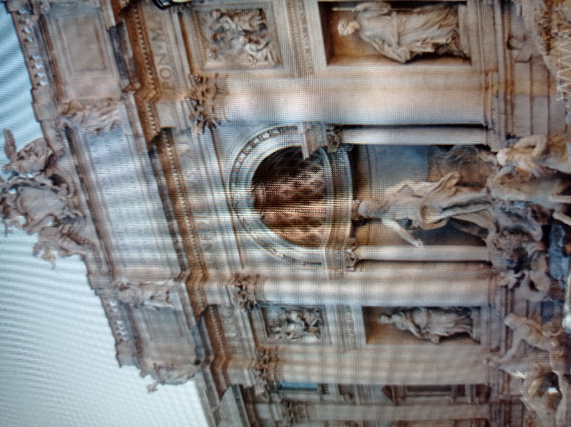 The image depicts the Trevi Fountain in Rome, Italy. It is a large Baroque fountain with intricate sculptures and architectural elements. The central figure is Neptune, god of the sea, standing in a shell-shaped chariot pulled by sea horses. Flanking him are other mythological figures and allegorical sculptures. The fountain is set against a grand facade with columns, niches, and relief sculptures. The water flows from various spouts into a large basin. The lighting suggests it is daytime. The location of Mukachevo, Ukraine is not present in the image.