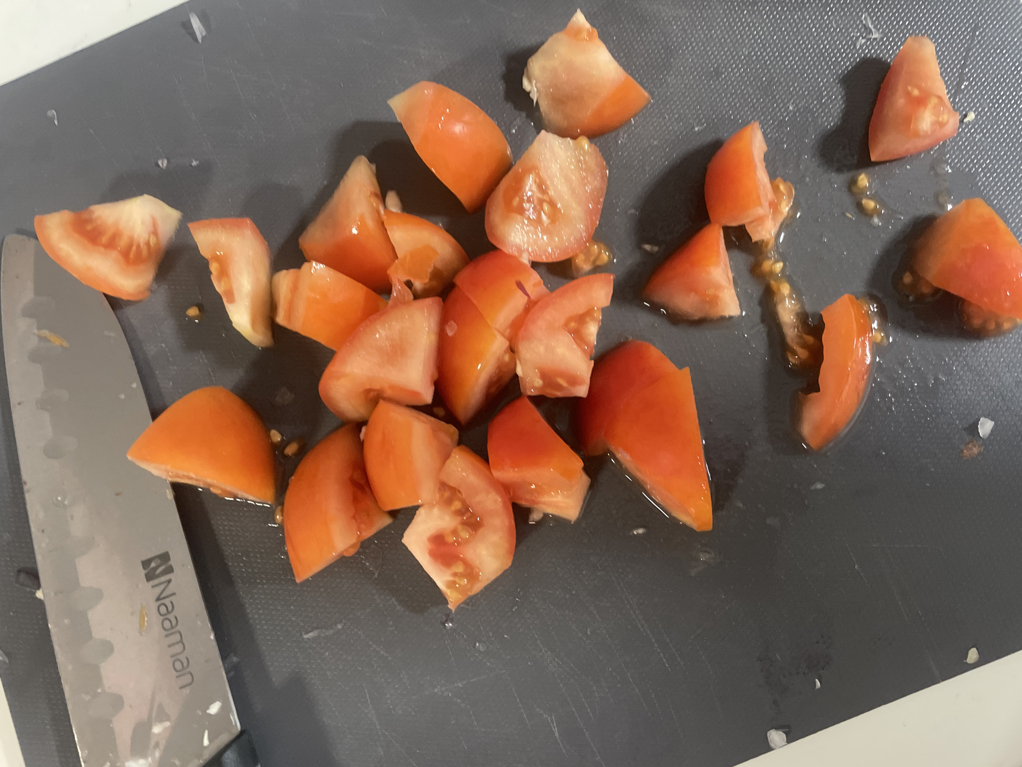 The image shows diced tomatoes on a gray cutting board with a "Naaman" knife partially visible on the left. The scene appears to be a food preparation setting. There is no indication that this image was taken in Raanana, Israel.