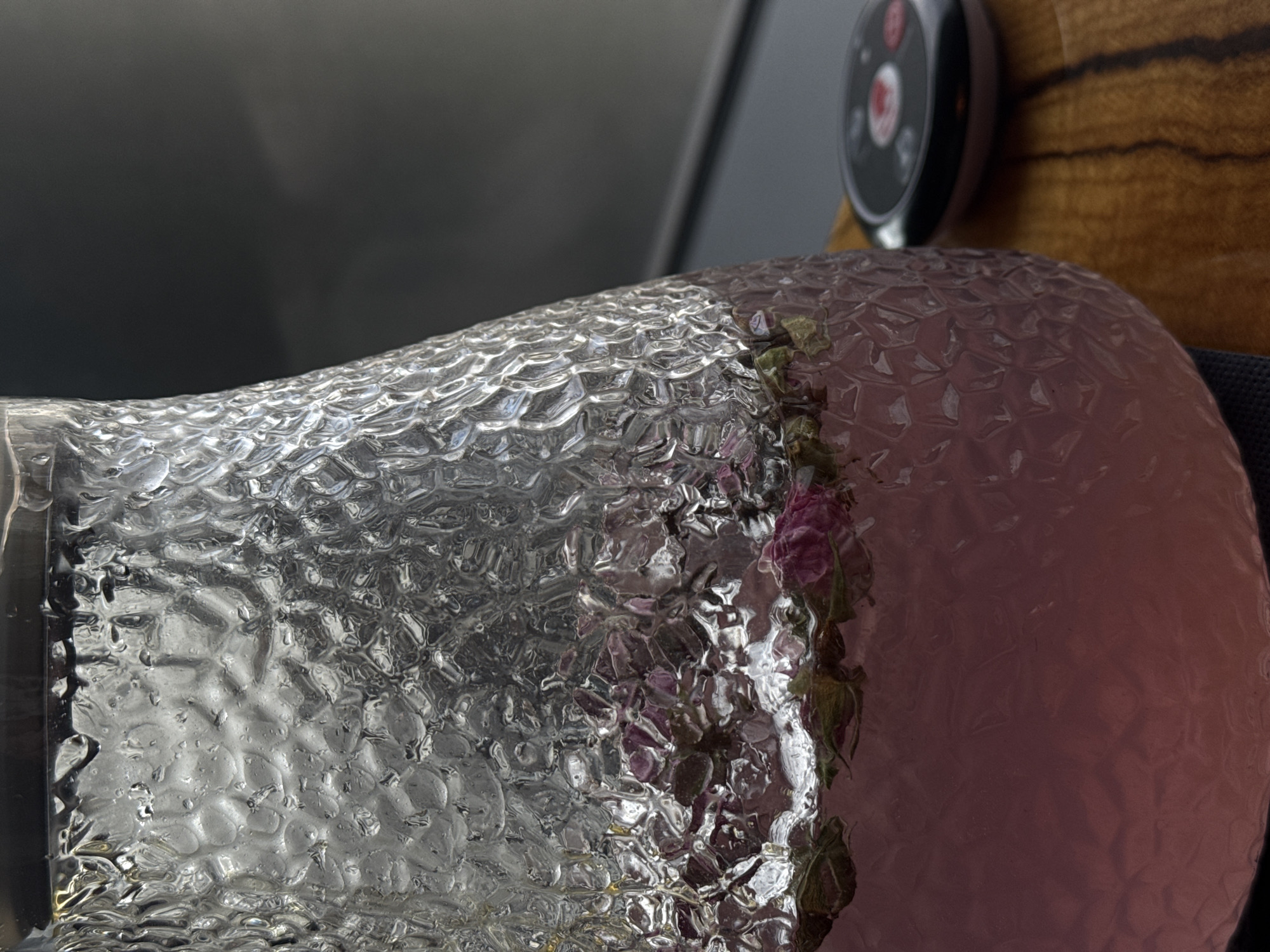 A close-up shows a textured glass vase with blurred pink flowers inside. A smart watch and a wooden surface are partially visible in the background. The location and specific setting within Krasnoyarsk, Russia, are not discernible from the image.