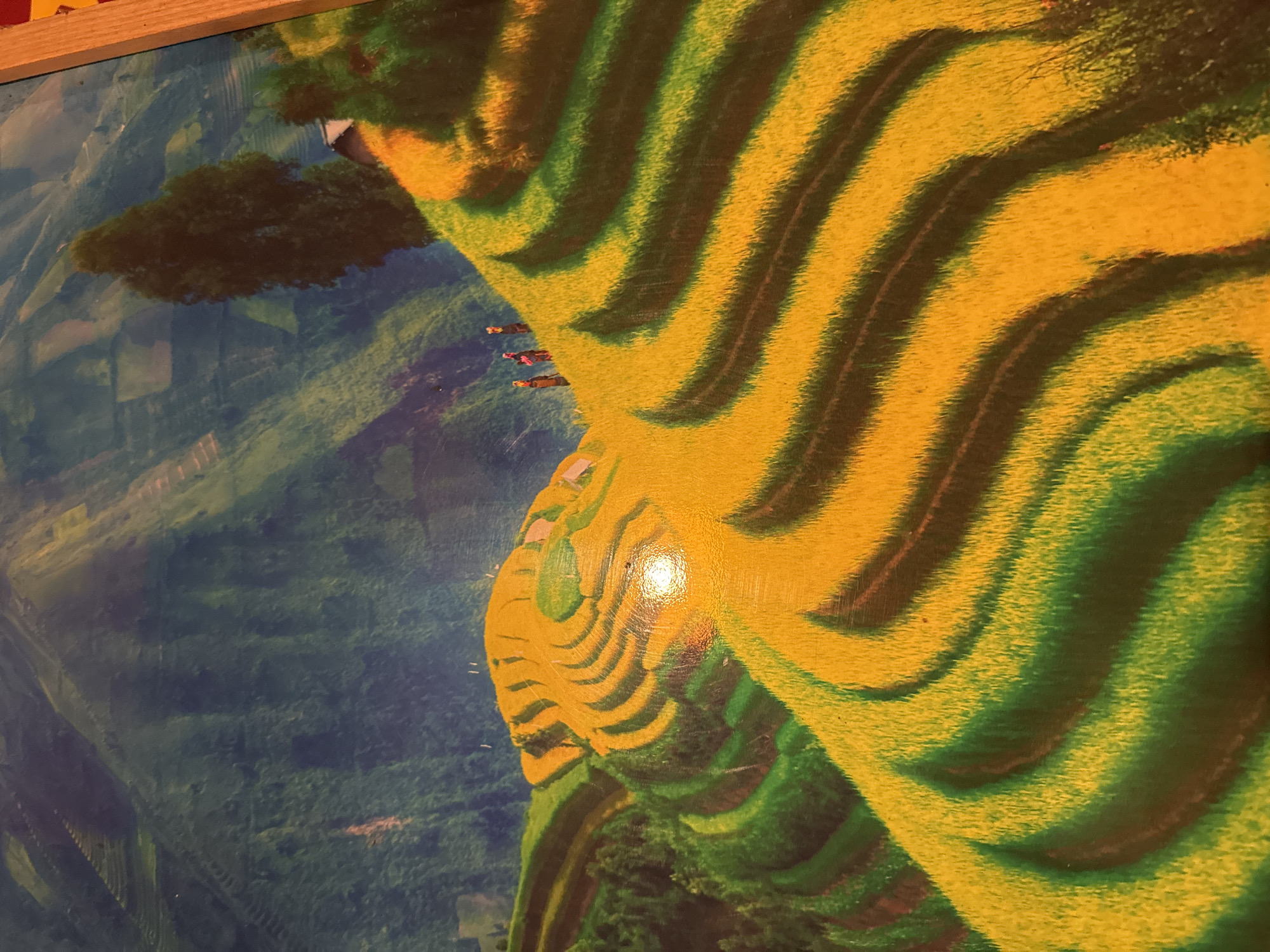 The image displays a mountainous agricultural landscape identified as the region of Ta Xua, Vietnam. Prominent in the foreground and mid-ground are extensive terraced fields, primarily covered with golden-yellow crops, indicative of ripe rice ready for harvest. These fields ascend steep slopes in curved, undulating patterns, with some terraces also exhibiting green vegetation.
In the mid-ground, on an upper golden-yellow terrace, three human figures are visible, walking in single file from left to right. They appear to be wearing dark clothing and carrying items on their backs. To the upper right, a solitary, tall, dark-foliaged tree stands prominently, partially obscuring a small structure with a dark roof and lighter walls nestled against the slope. The background consists of multiple layers of distant mountains, appearing dark green and blue-tinged, suggesting further terraced areas or natural forestation. A bright, circular light reflection is present on the surface of the image in the lower-middle section.