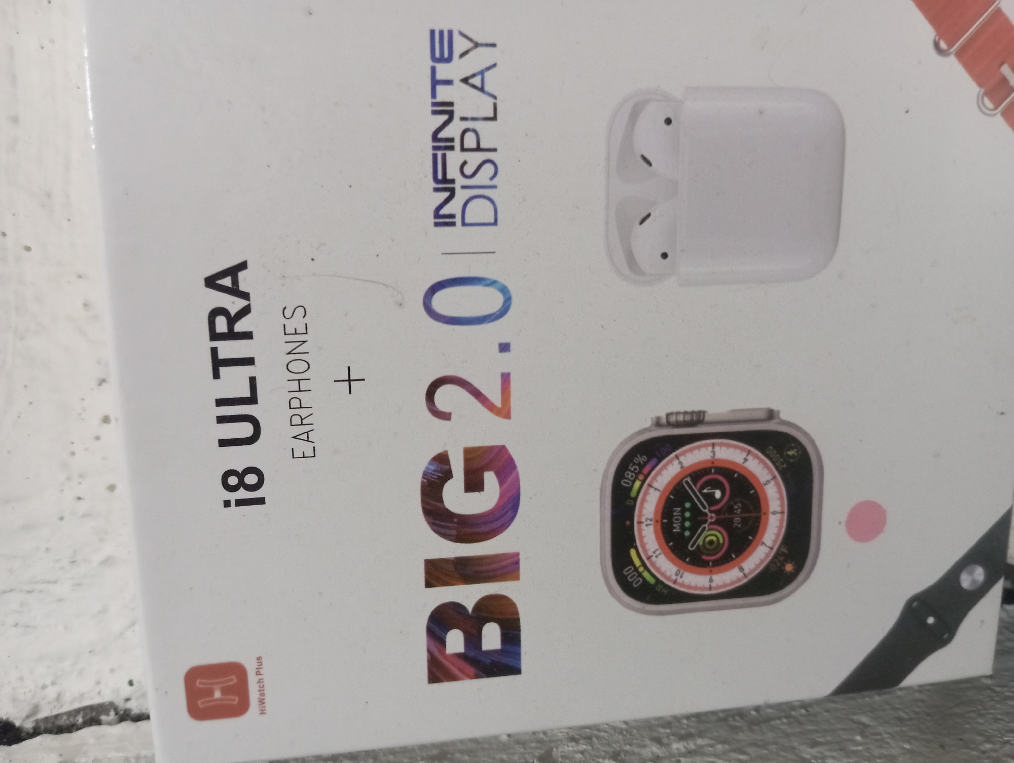 This image showcases the packaging for an "i8 ULTRA EARPHONES" product. The packaging features a prominent "HiWatch Plus" logo. Text on the box reads "BIG 2.0" and "INFINITE DISPLAY," suggesting a large screen or a new generation of the product. An image of a smartwatch with a colorful digital display and a pair of white wireless earbuds in their charging case are also depicted on the packaging. The background appears to be a textured, light-colored wall, possibly brick, with some dirt or scuff marks. This scene is not located in Rejosari, Indonesia; it is a product image on a white box.