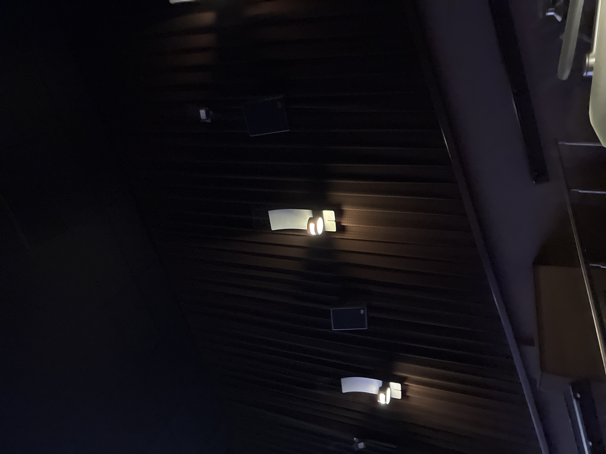 A low-angle shot of a dark, horizontally ribbed ceiling, likely indoors, features several recessed lights. Some of the lights are rectangular and illuminated. A black square object is also visible on the ceiling. The ceiling appears to be part of a building interior, but without further context, the specific location in Mexico City is undetermined.