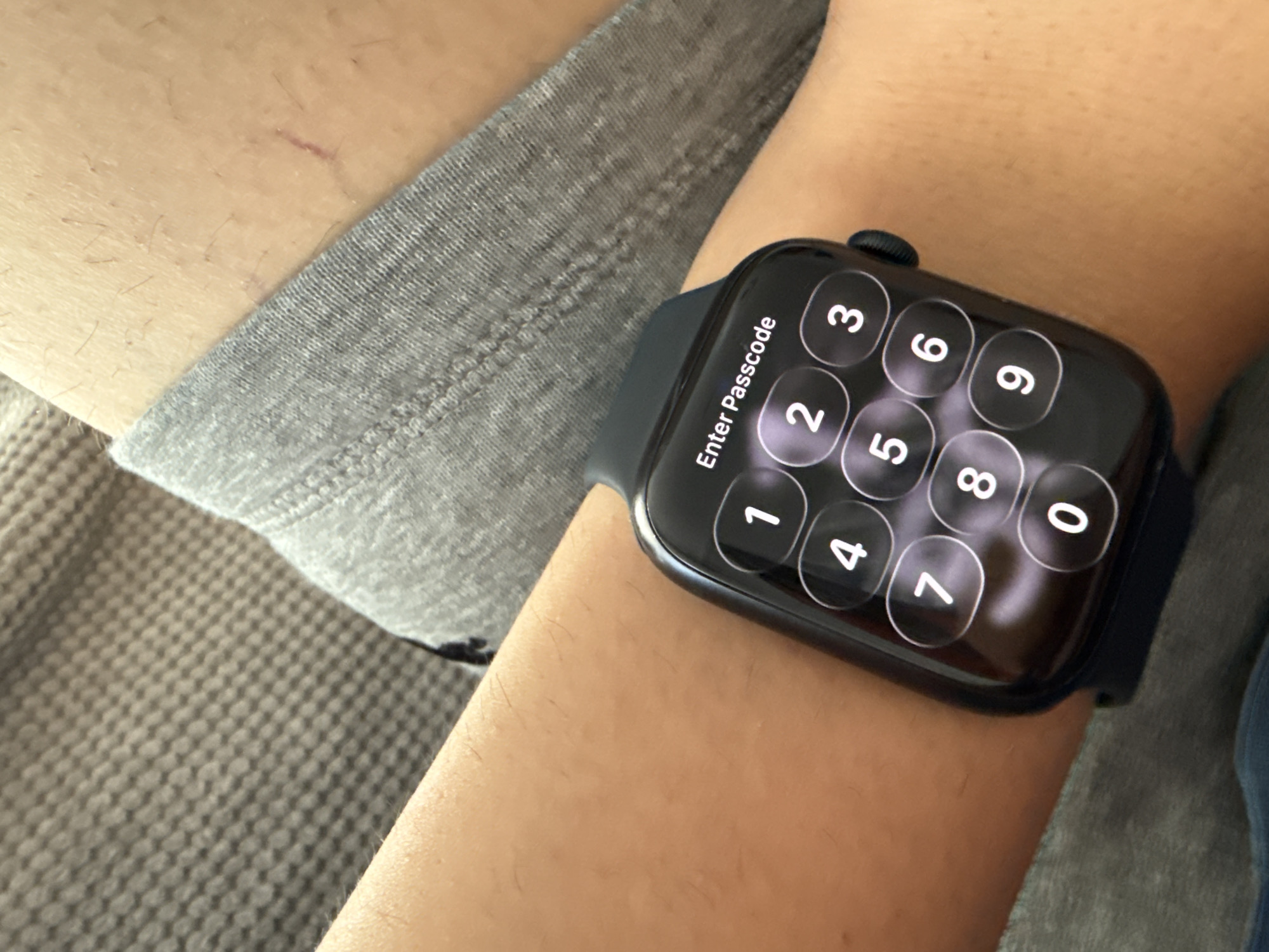 An Apple Watch is displayed on a person's wrist. The watch screen shows a numeric keypad with the prompt "Enter Passcode." The watch has a dark band and is positioned on the inner side of the wrist. The person is wearing a gray garment. A faint scar is visible on the wrist. The image does not provide any information about the location in the city of Lovech, Bulgaria.