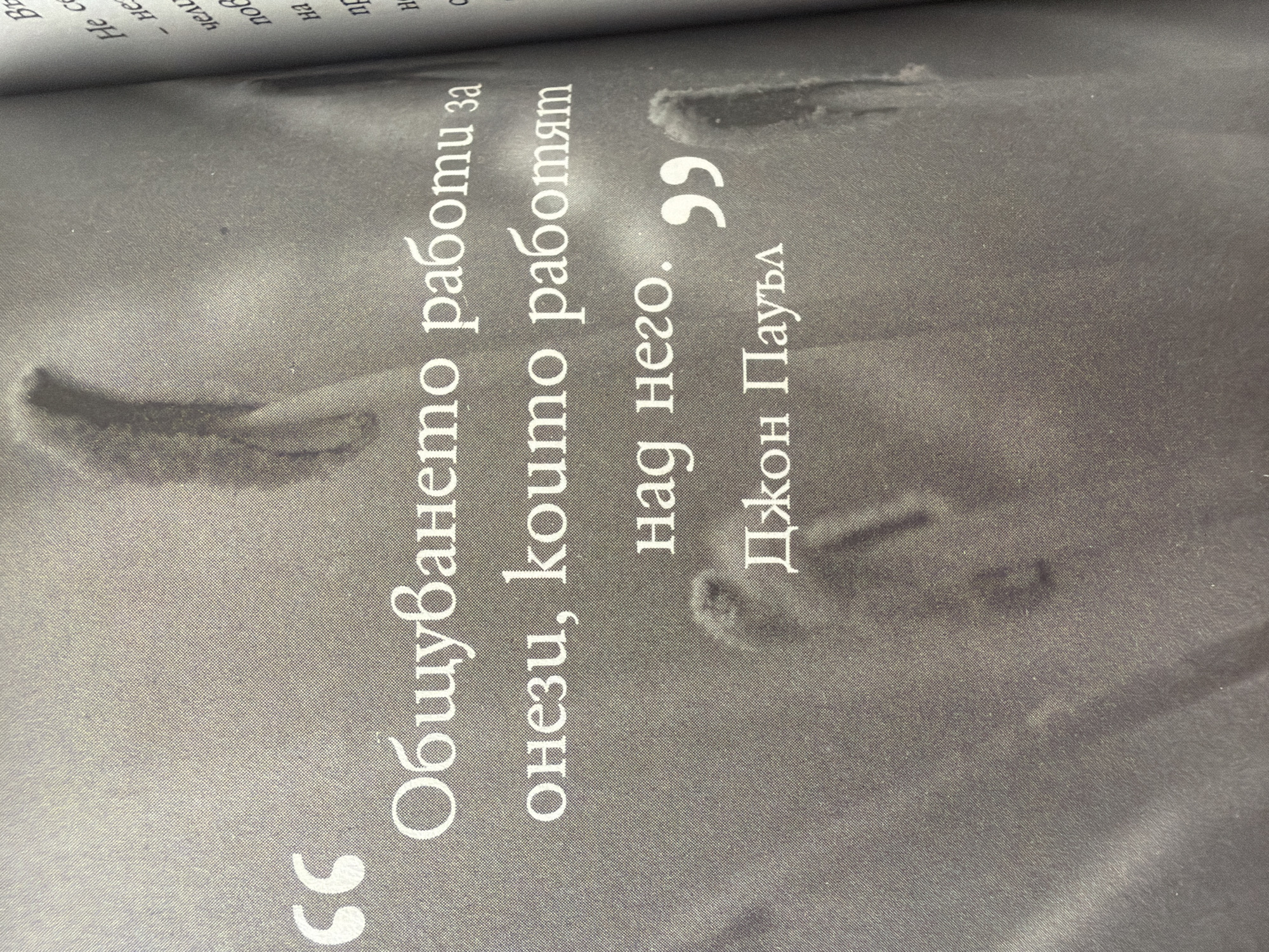 The image displays a quote in Bulgarian text, overlaid on a textured, grayscale background that appears to be a photograph of some organic or natural elements, possibly dried plant stalks. The quote is framed by quotation marks and is attributed to "Джон Паул" (John Paul). The text is in a serif font and reads: "Общуването работи за онези, koumo работят над него." followed by the attribution. The background is out of focus, suggesting a shallow depth of field. The lighting is soft and diffused. There is no indication of the city of Pazardzhik, Bulgaria, in the image itself.
