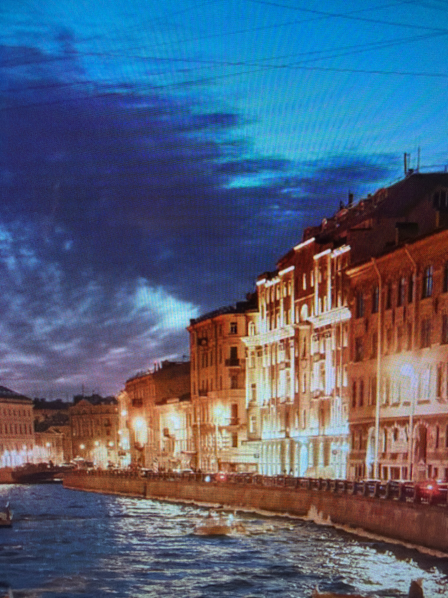 This media file depicts a nighttime cityscape with a river in the foreground. Ornate buildings with illuminated windows line the riverbank, casting a warm glow on the water's surface. The sky above is a deep blue, transitioning to a lighter shade towards the horizon, with dramatic clouds creating textured patterns. The architecture suggests a European setting, characterized by its grand scale and detailed facades.

The scene appears to be a busy urban environment, with lights suggesting a vibrant atmosphere. The river reflects the city lights, creating a shimmering effect. The overall mood is one of quiet elegance and nighttime beauty. There are no visible people or specific objects that stand out prominently, focusing instead on the architectural grandeur and the interplay of light and shadow. The time of day is clearly nighttime, as indicated by the artificial lighting of the buildings and the dark sky. The weather appears to be clear, allowing for a visible sky. While no specific text is visible, the overall visual composition conveys a sense of history and urban life. The location context provided is Kafr Yasif, Israel, which doesn't seem to directly correlate with the visual elements of a European-style cityscape.