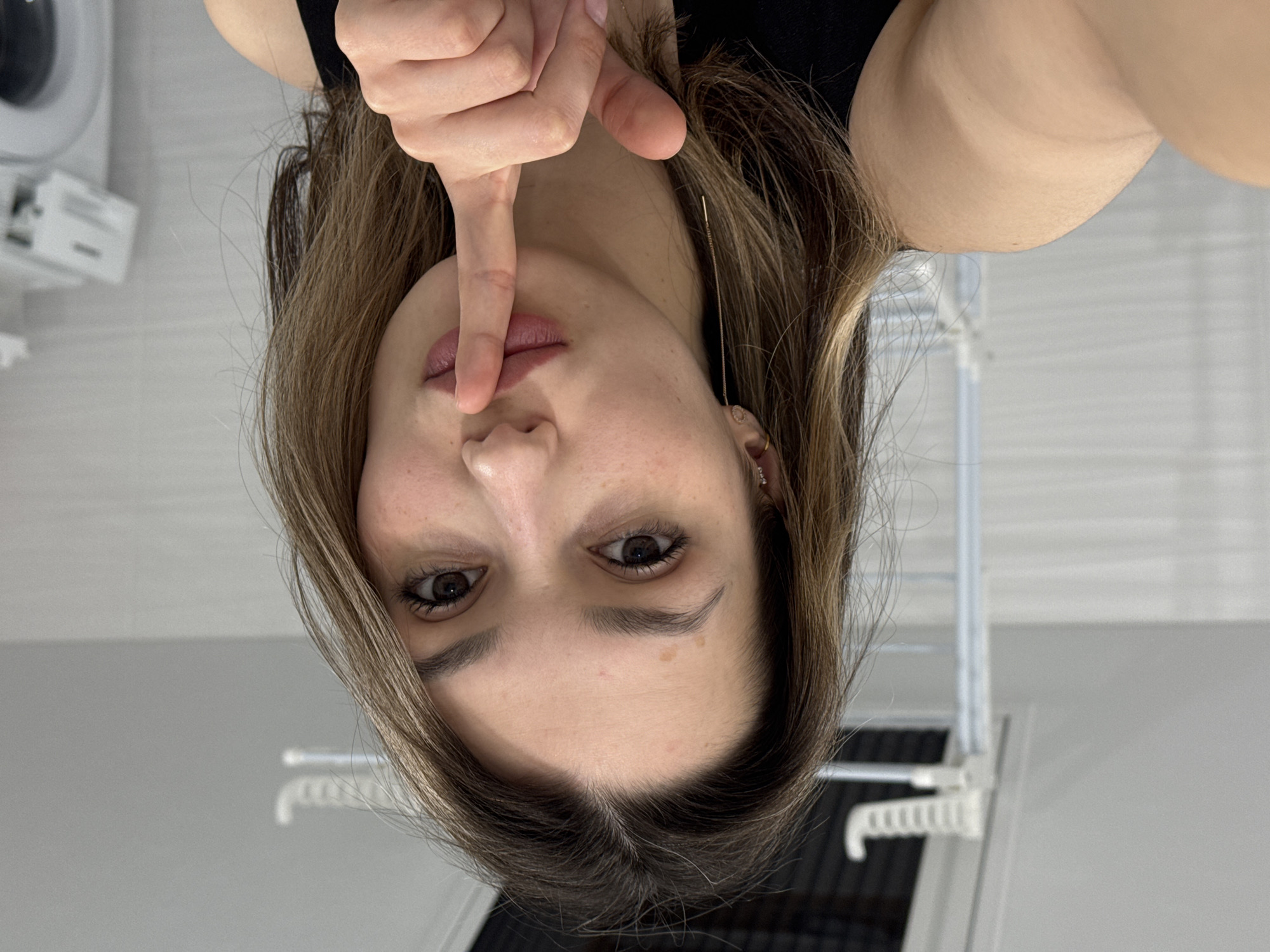 A woman is holding her index finger to her lips. The environment is nondescript.