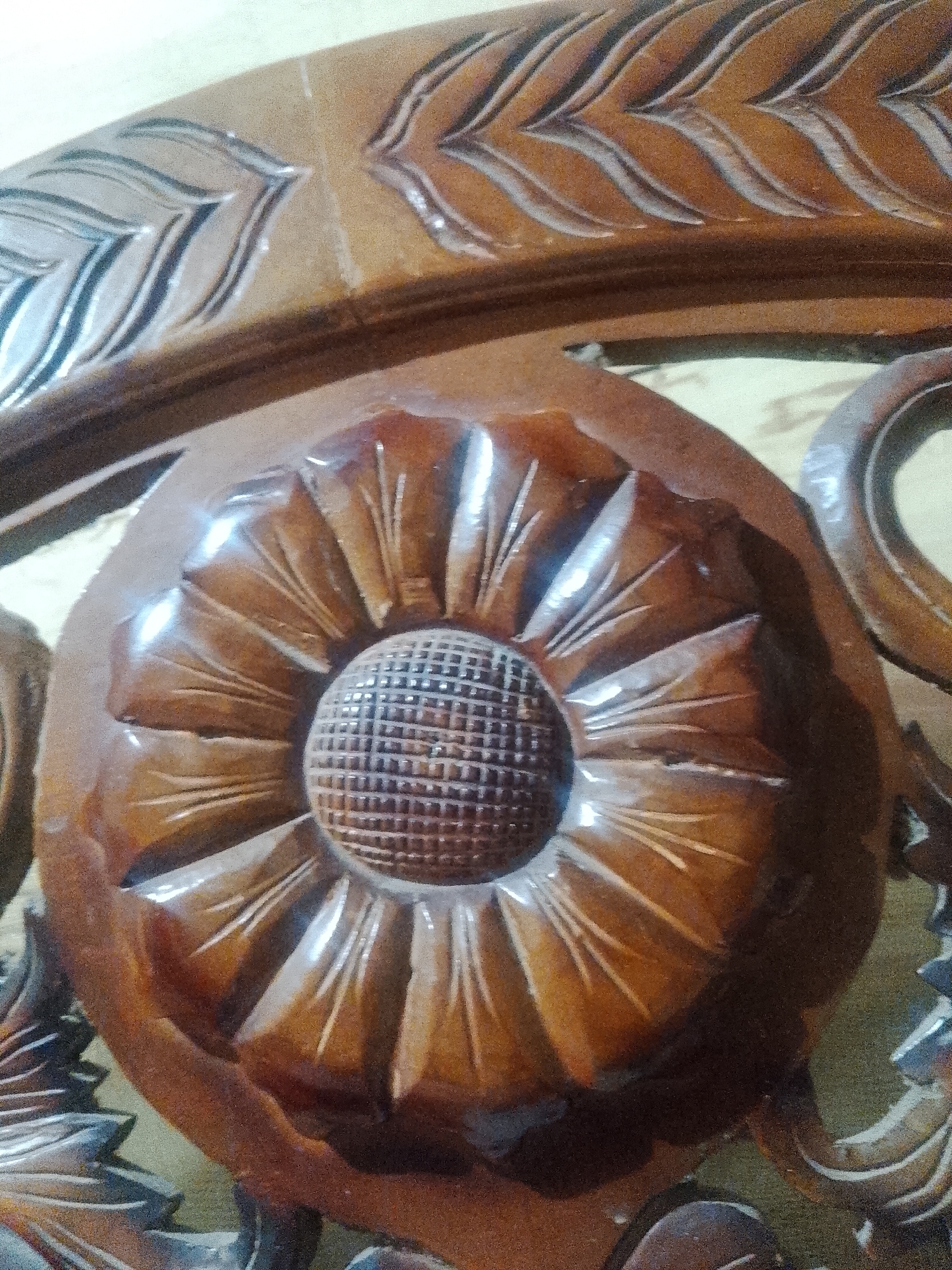 A close-up shot showcases detailed wood carvings. A circular element resembling a flower dominates the center, with textured petals radiating from a gridded center. The surrounding wood features leaf-like carvings. The image does not provide information about the city of Lhokseumawe, Indonesia, or any people, actions, or interactions.