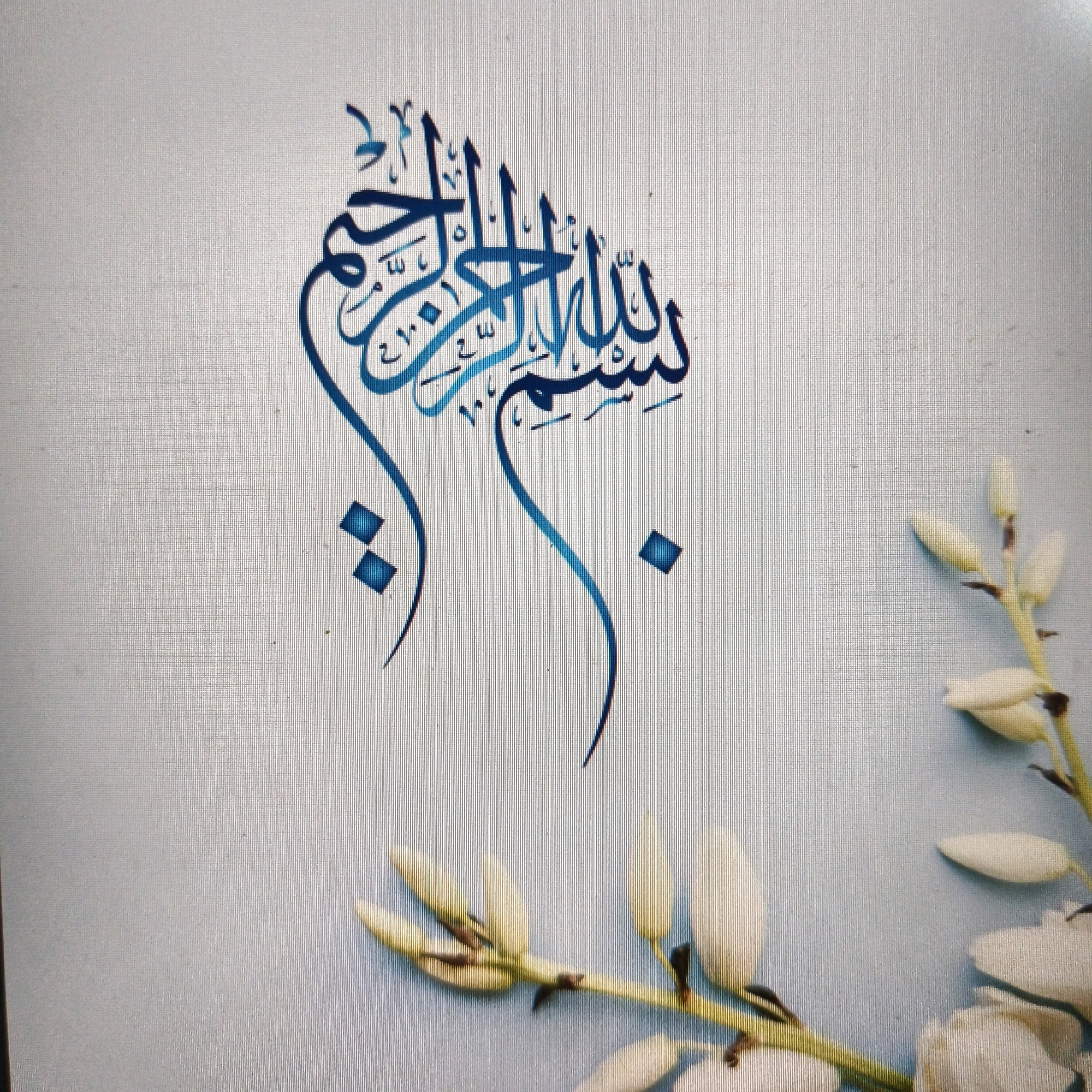 The image is a close-up of Arabic calligraphy, specifically the phrase "Bismillah al-Rahman al-Rahim" (In the name of Allah, the Most Gracious, the Most Merciful). The calligraphy is rendered in a gradient of blue, with darker shades forming the main lines and lighter shades filling in the curves. The script is ornate and flowing. Behind the calligraphy, the background is a textured, light blue surface, possibly paper or fabric, with a subtle grid pattern. In the lower right corner, a sprig of white, unopened flower buds is visible, adding a touch of nature to the composition. There is no indication of the city of Poonch, India, in the image.