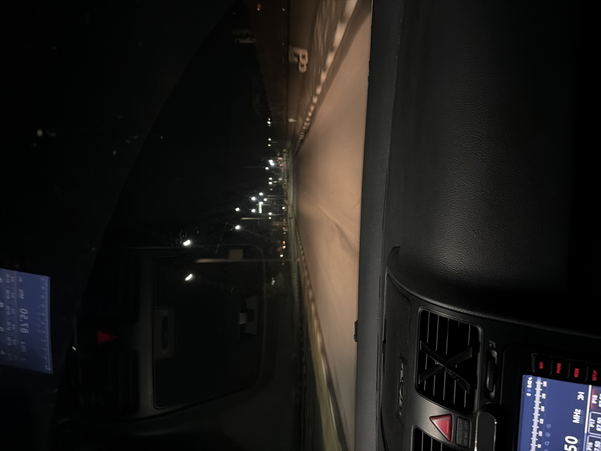 The image shows a view from inside a vehicle at night. The vehicle is on a road lined with streetlights. The road appears to be wide, and there is a visible 'P' marking on the road. A digital display is seen inside the vehicle, showing radio frequency information. The location is possibly in the city of Galabovo, Bulgaria.
