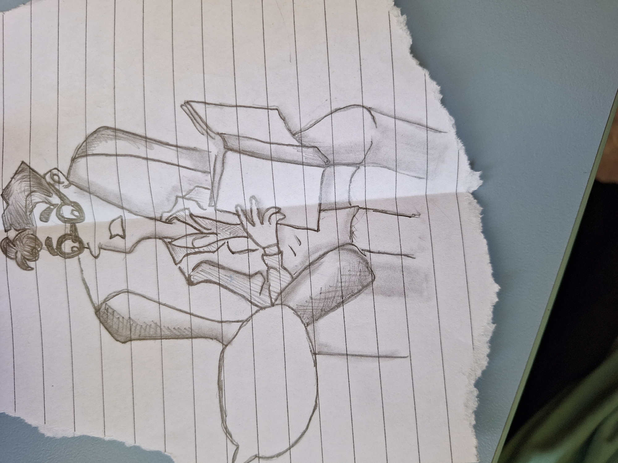 A pencil sketch on lined paper depicts a person engrossed in reading a book. The person is seated in a chair, wearing glasses and a suit jacket over a collared shirt. Their hair is styled in a bun. The sketch is partially torn along the bottom edge. The background is a plain surface, likely a table. The sketch does not contain any information that would allow for its localization to Varna, Bulgaria, or any other specific geographical location.