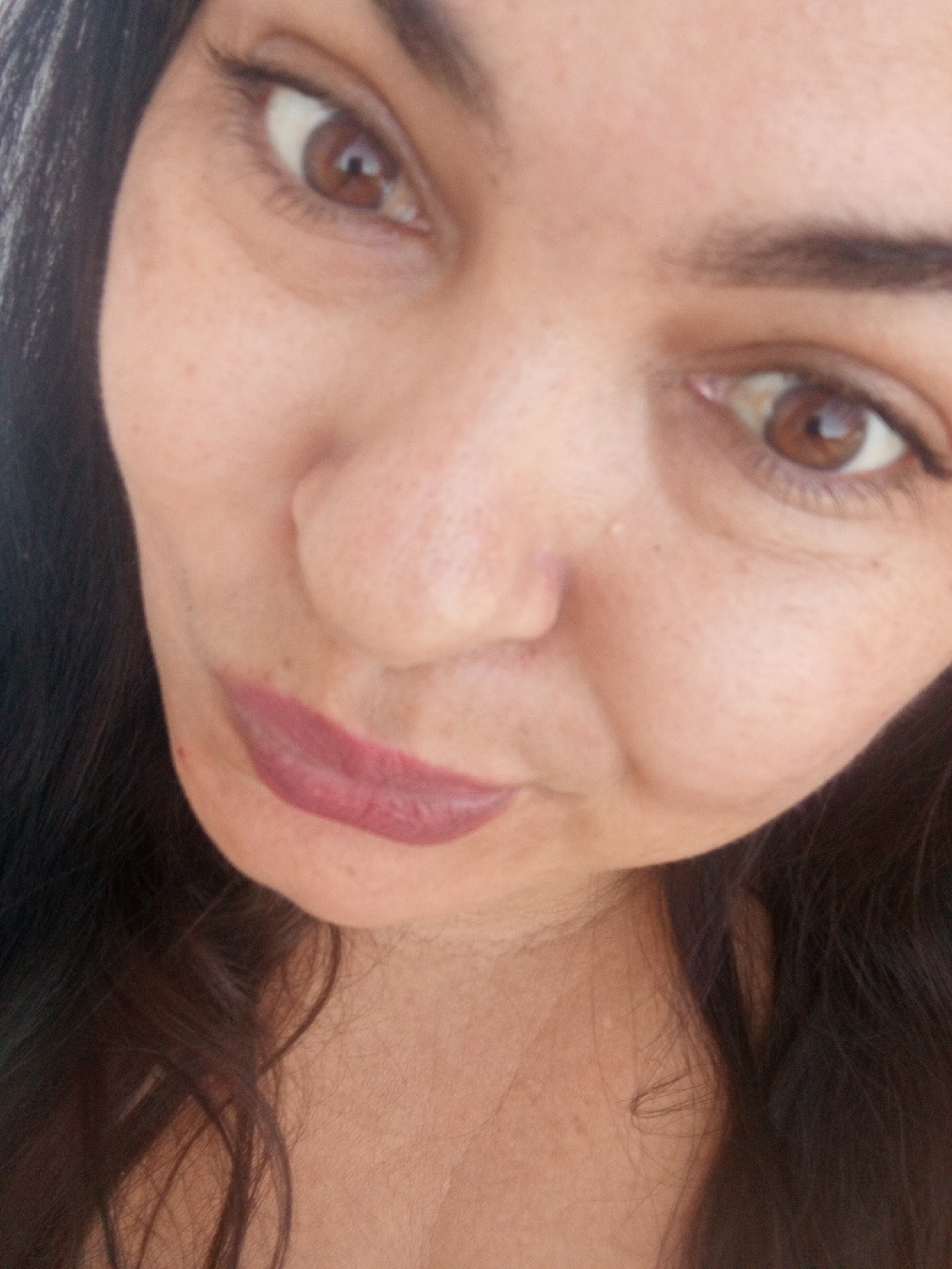 A close-up photo of a woman's face is presented at a skewed angle, capturing her features from slightly below. Her brown eyes are prominent, contrasting with her light-toned skin. Her lips are pursed and colored with a mauve lipstick. Dark brown hair frames her face. The background and wider context, including any location such as Juan Griego, Venezuela, are not visible.